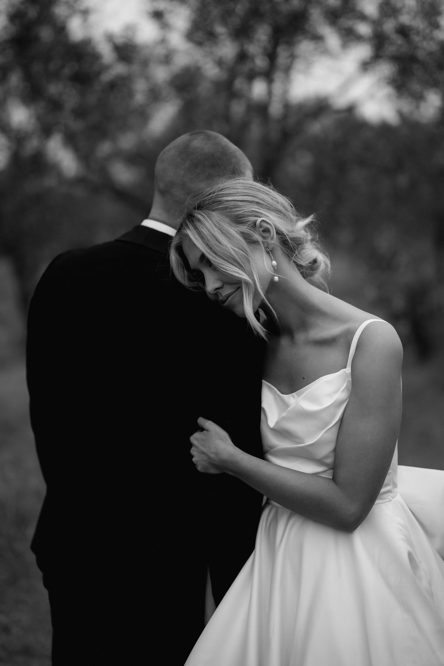 A tender black and white wedding photograph shows a couple embracing, with the bride in white leaning against her partner's shoulder.