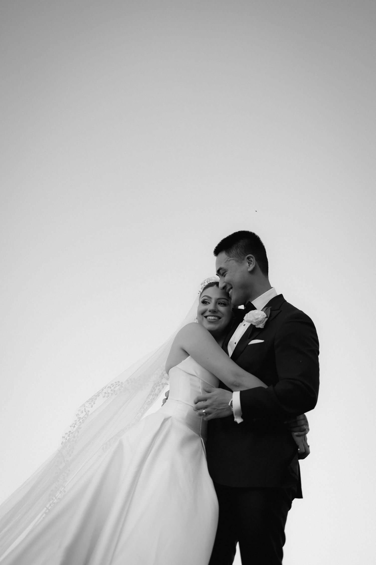 A romantic black and white portrait of newlyweds embracing against a minimalist background.