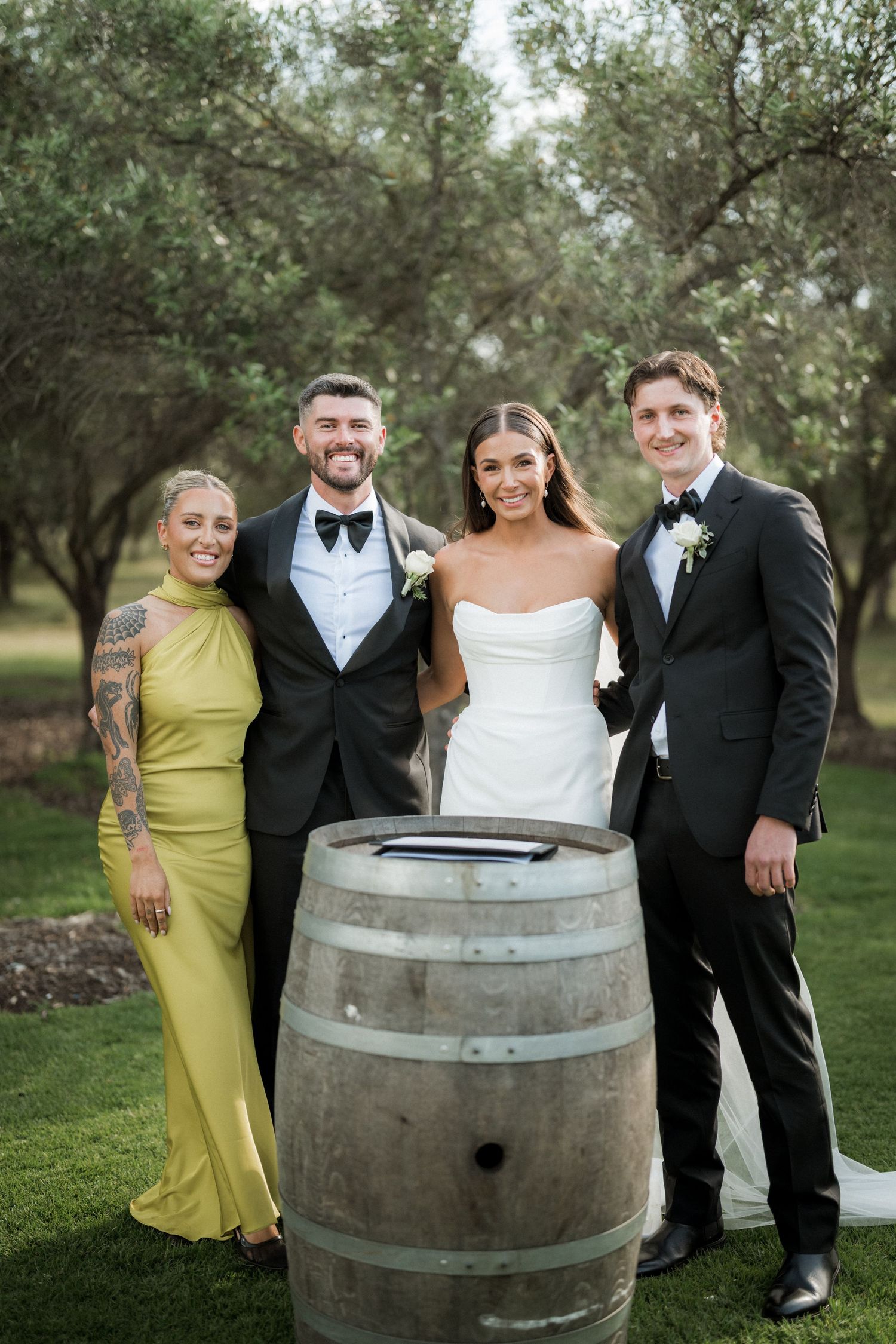 Wedding party posing casually around a rustic wine barrel outdoors.