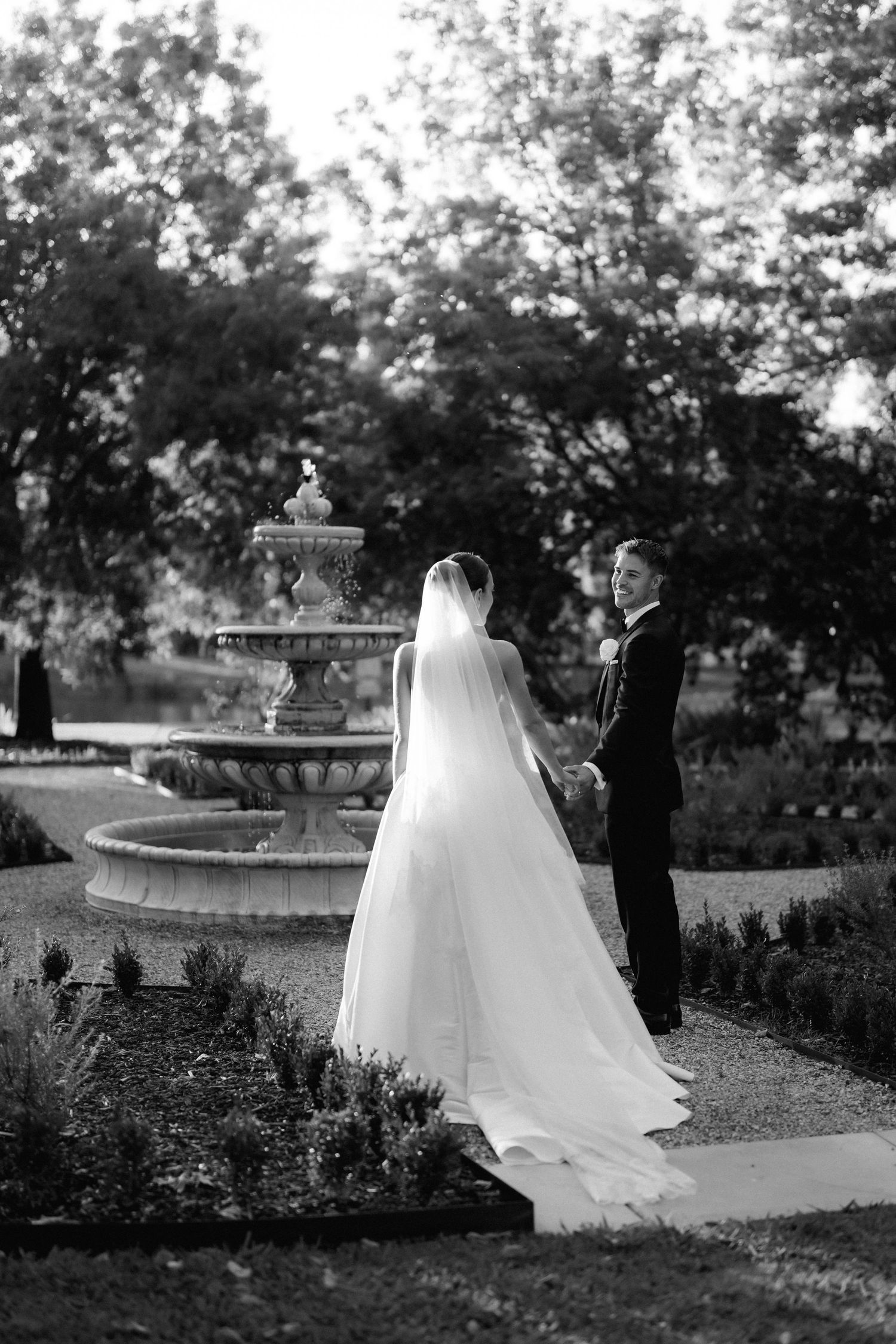 Black and white wedding photos showing a bride in flowing white dress near a garden fountain.