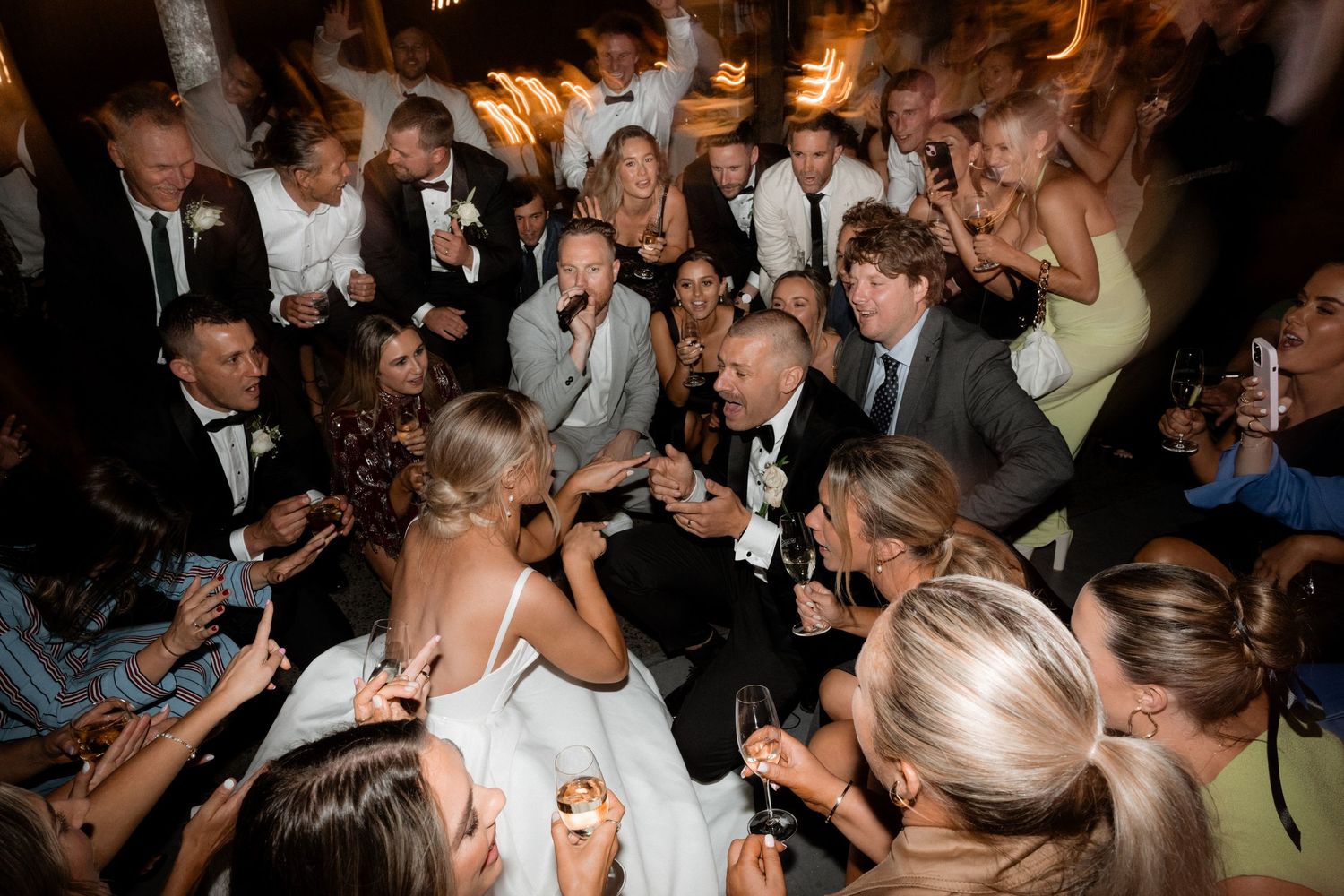 Energetic crowd dancing and celebrating at a dimly lit wedding reception.