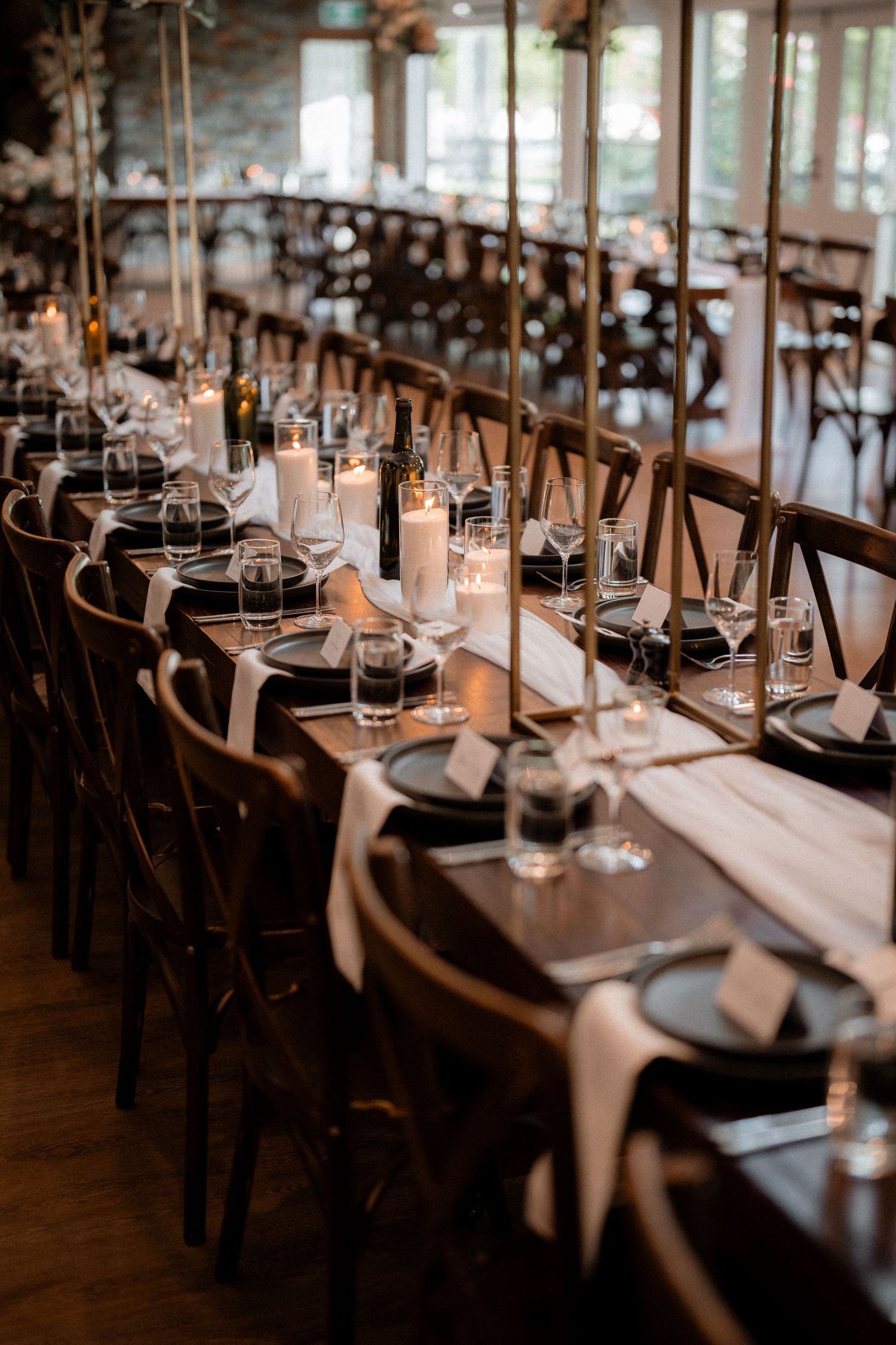 Elegant wedding reception tables set with candles and place settings in a rustic indoor venue.