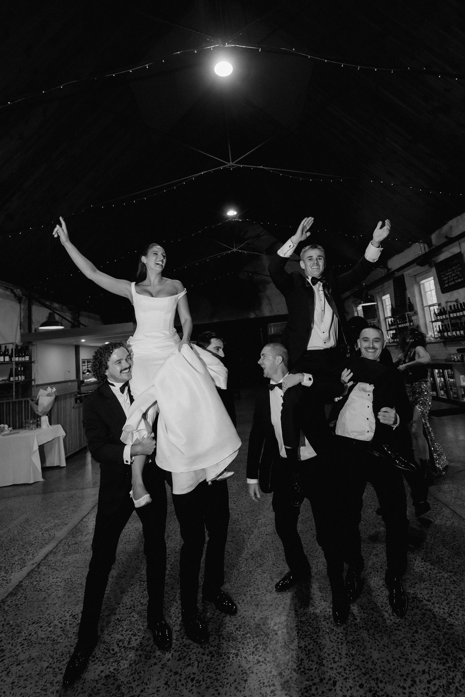 Wedding guests dance and celebrate on a dark dance floor under string lights at night.