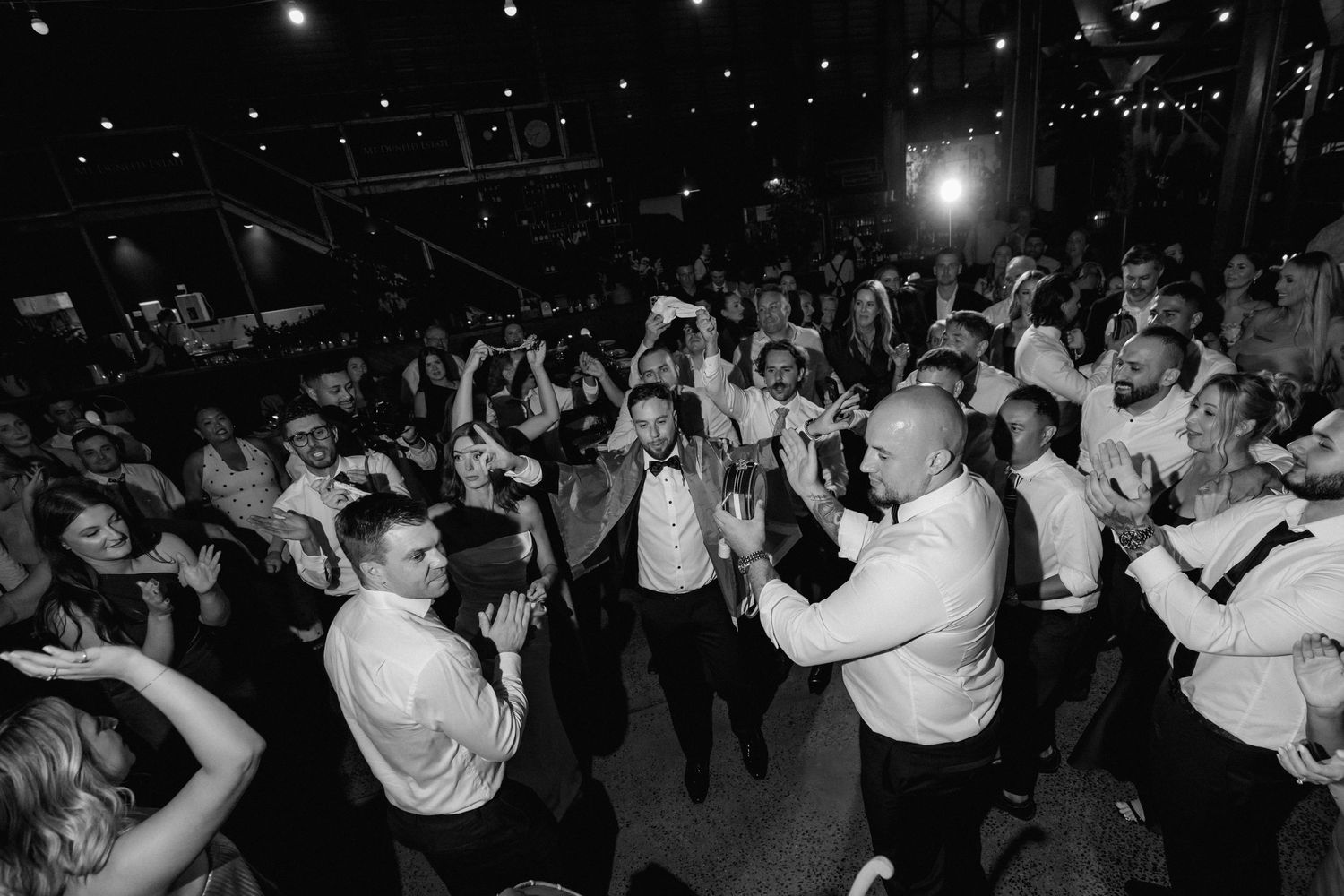 Black and white photo of people dancing and celebrating at a lively party or reception.