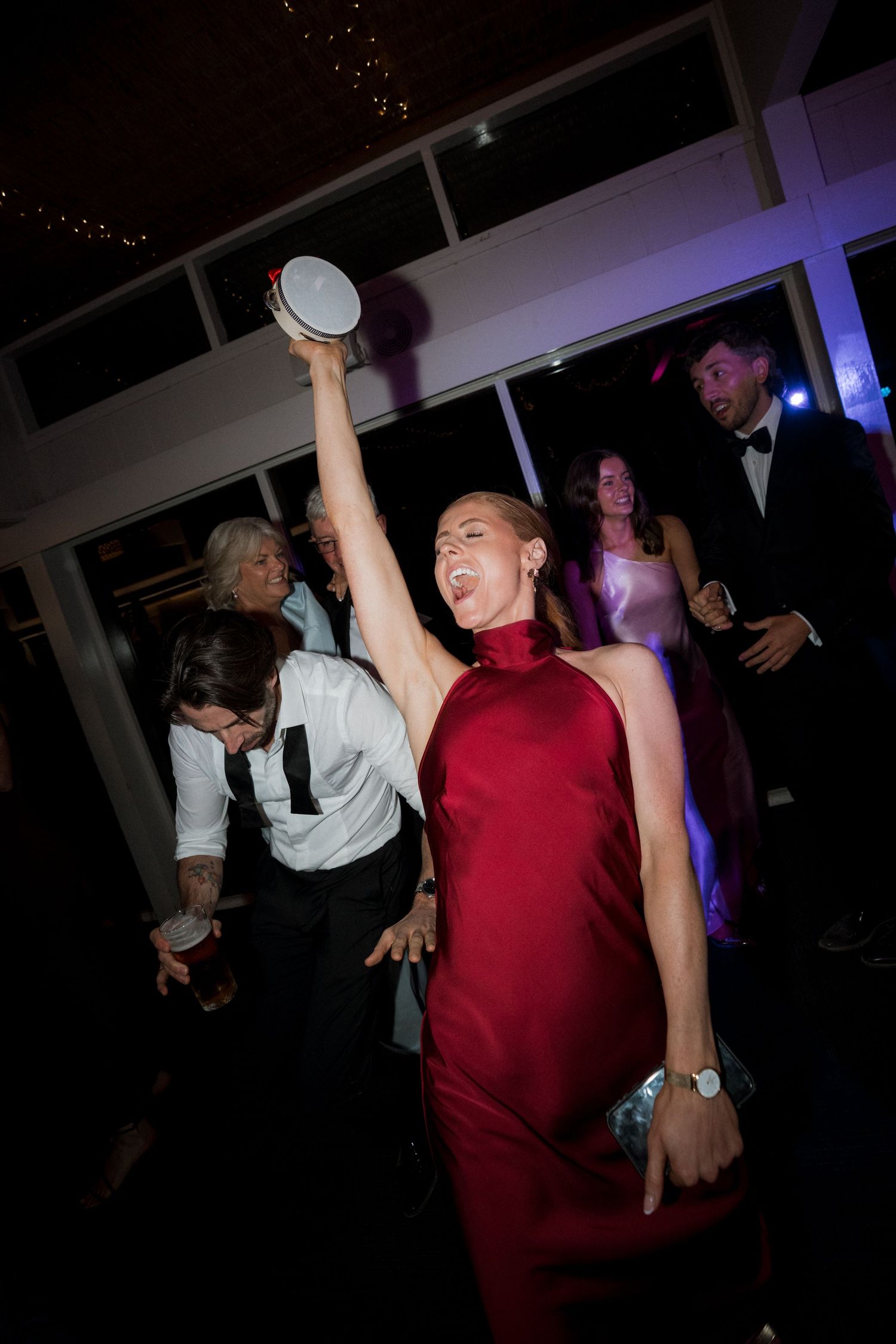 Wedding reception guests dance energetically under dark lighting with arms raised.