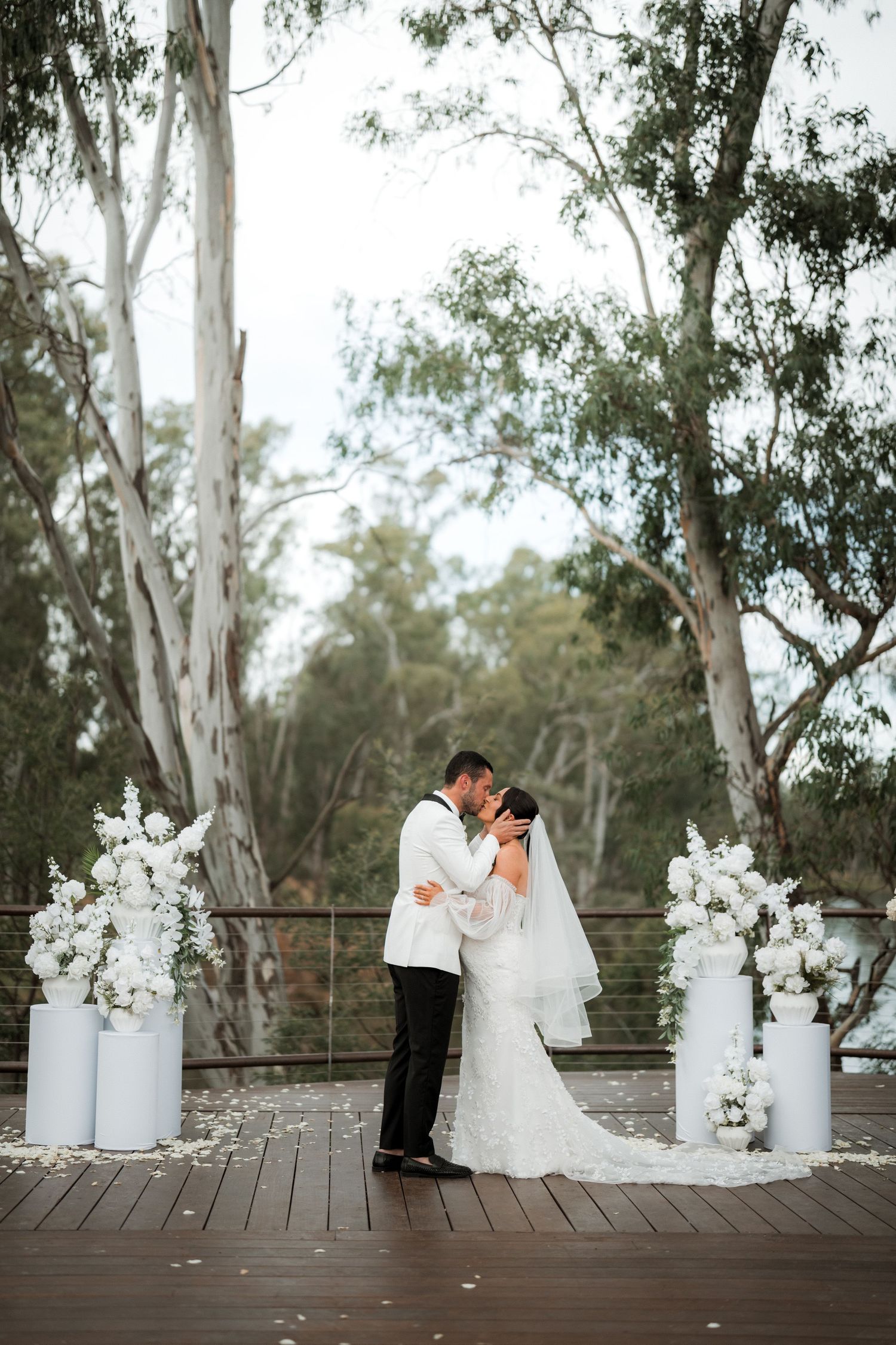 Elegant outdoor wedding scene with white floral arrangements and eucalyptus trees creating a natural backdrop.
