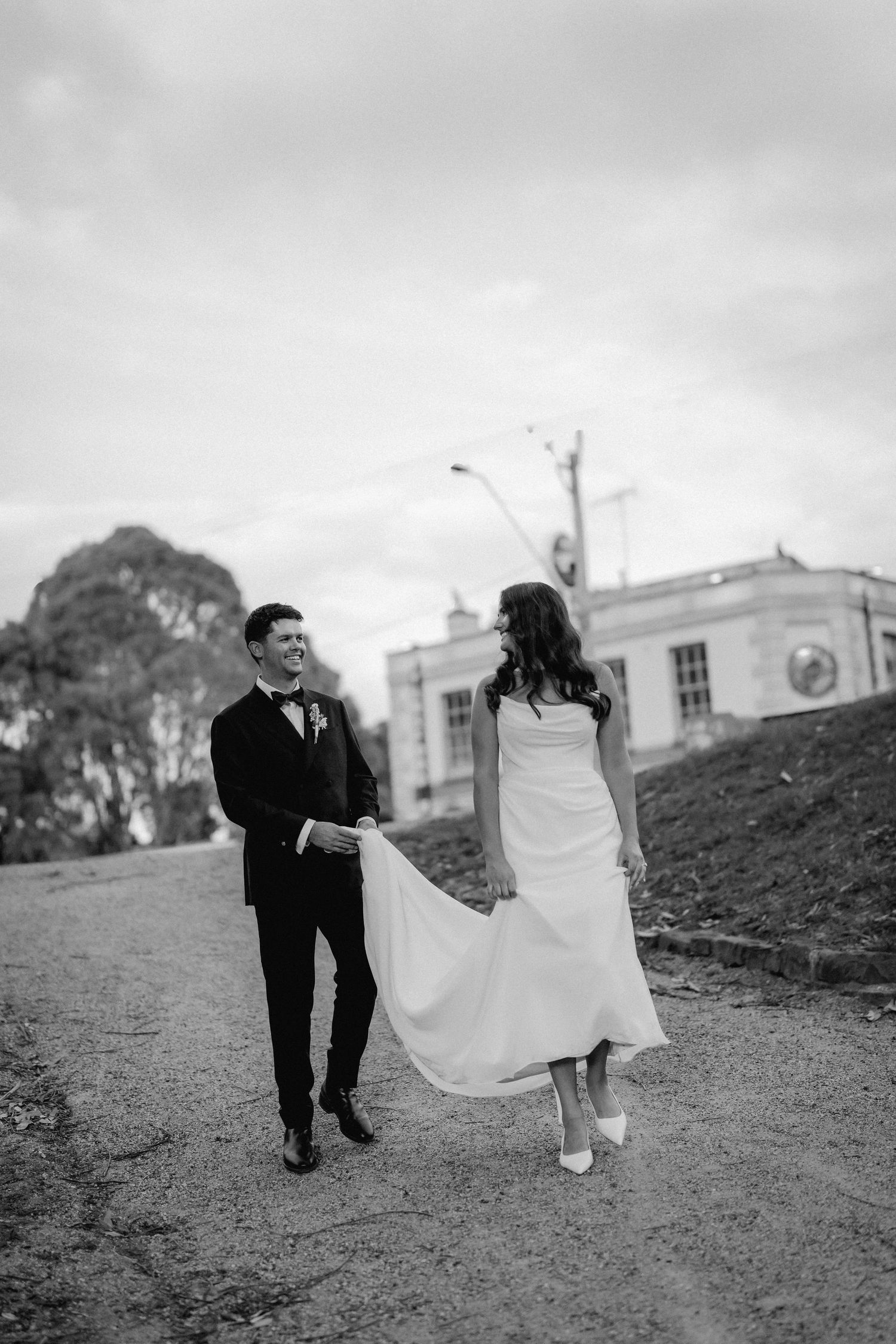 Black and white wedding photo of couple walking playfully on a hillside.