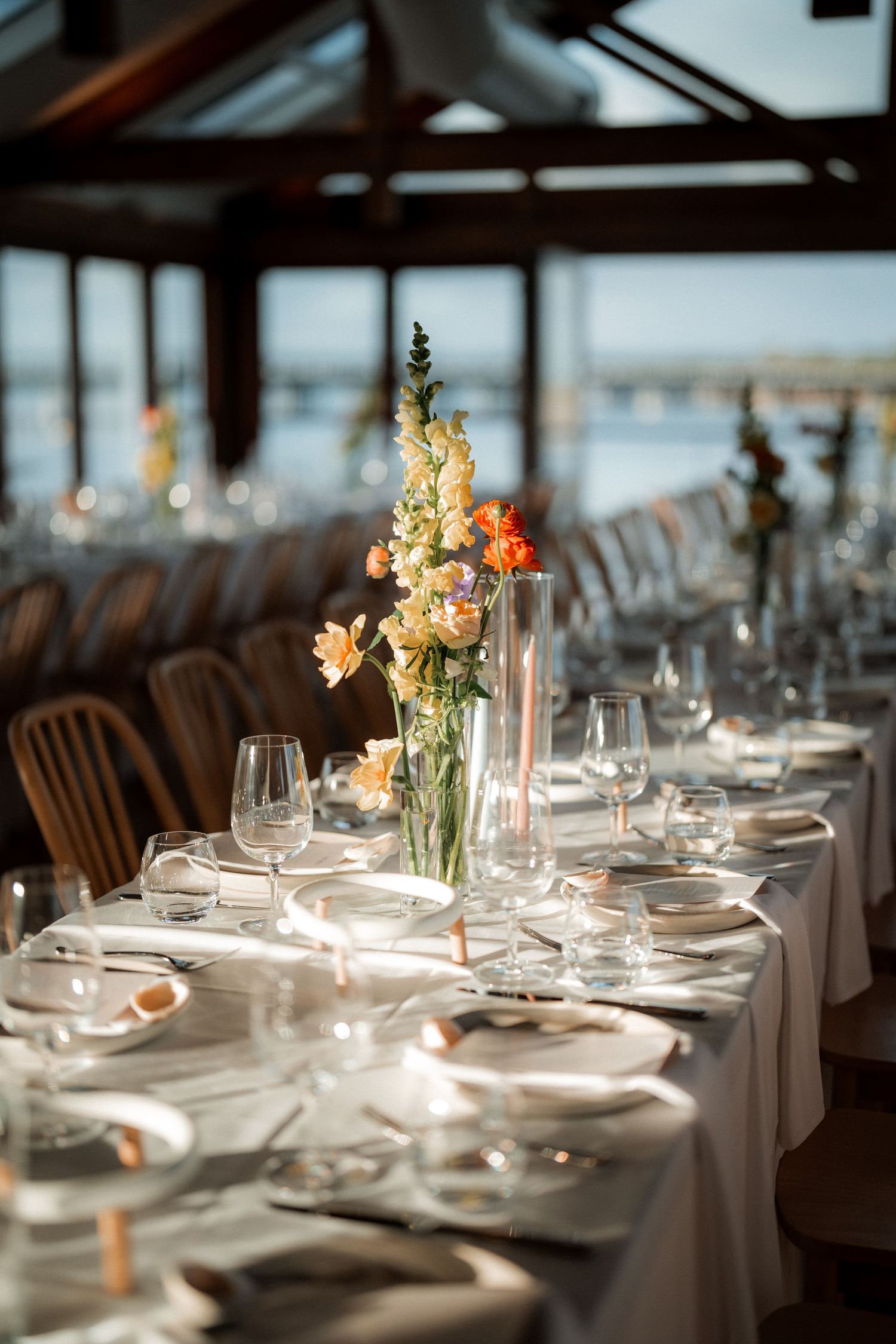 Elegant wedding reception tables set with white linens and floral centerpieces in rustic venue.