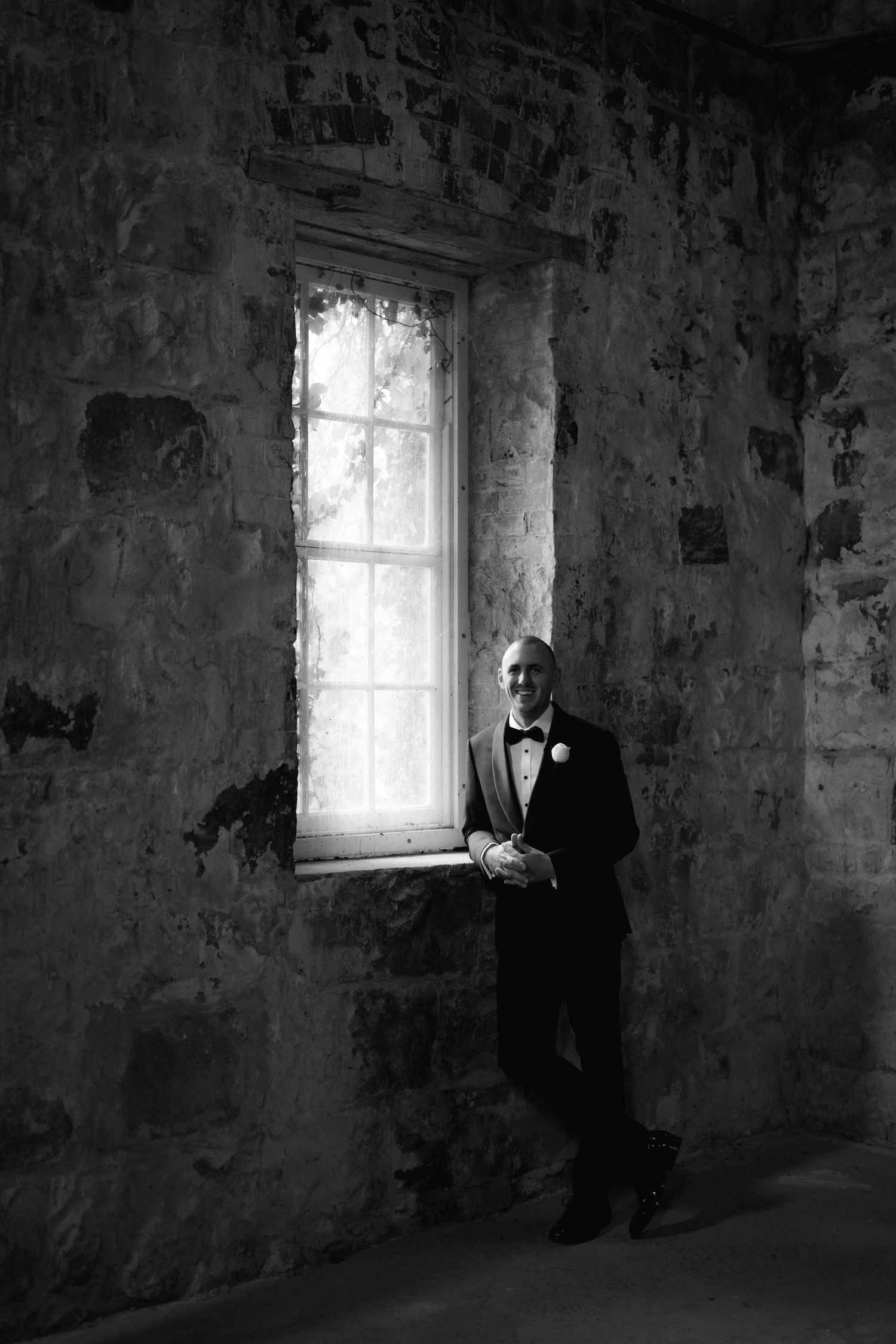 Series of moody black and white photos showing a figure standing by a window in an old stone room.