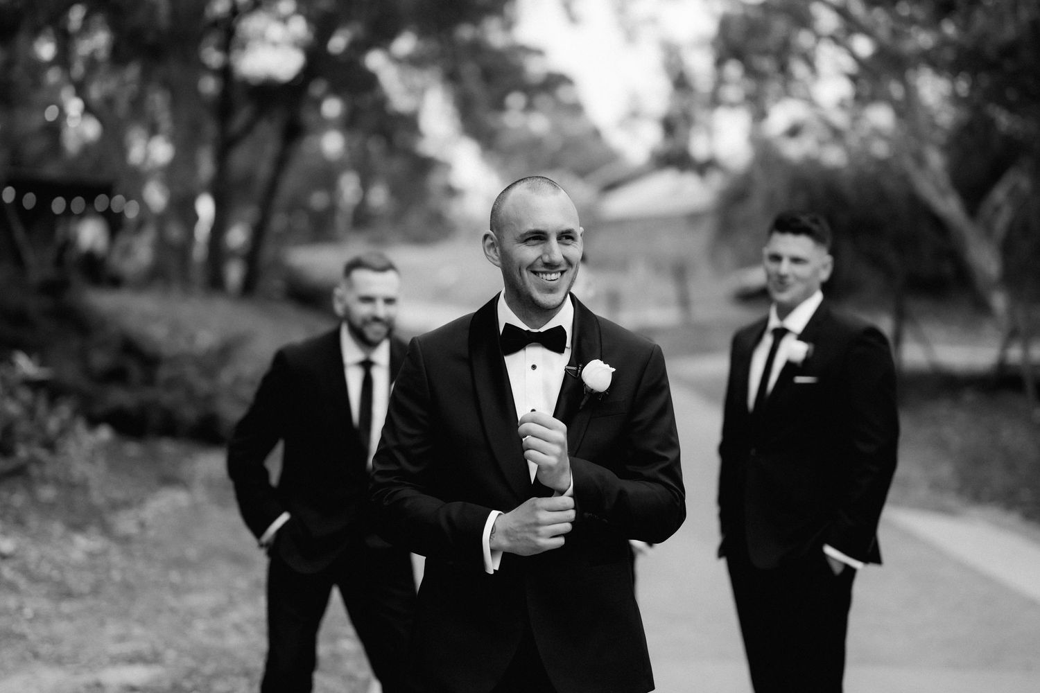 Groomsmen in black tuxedos share a candid moment outdoors.