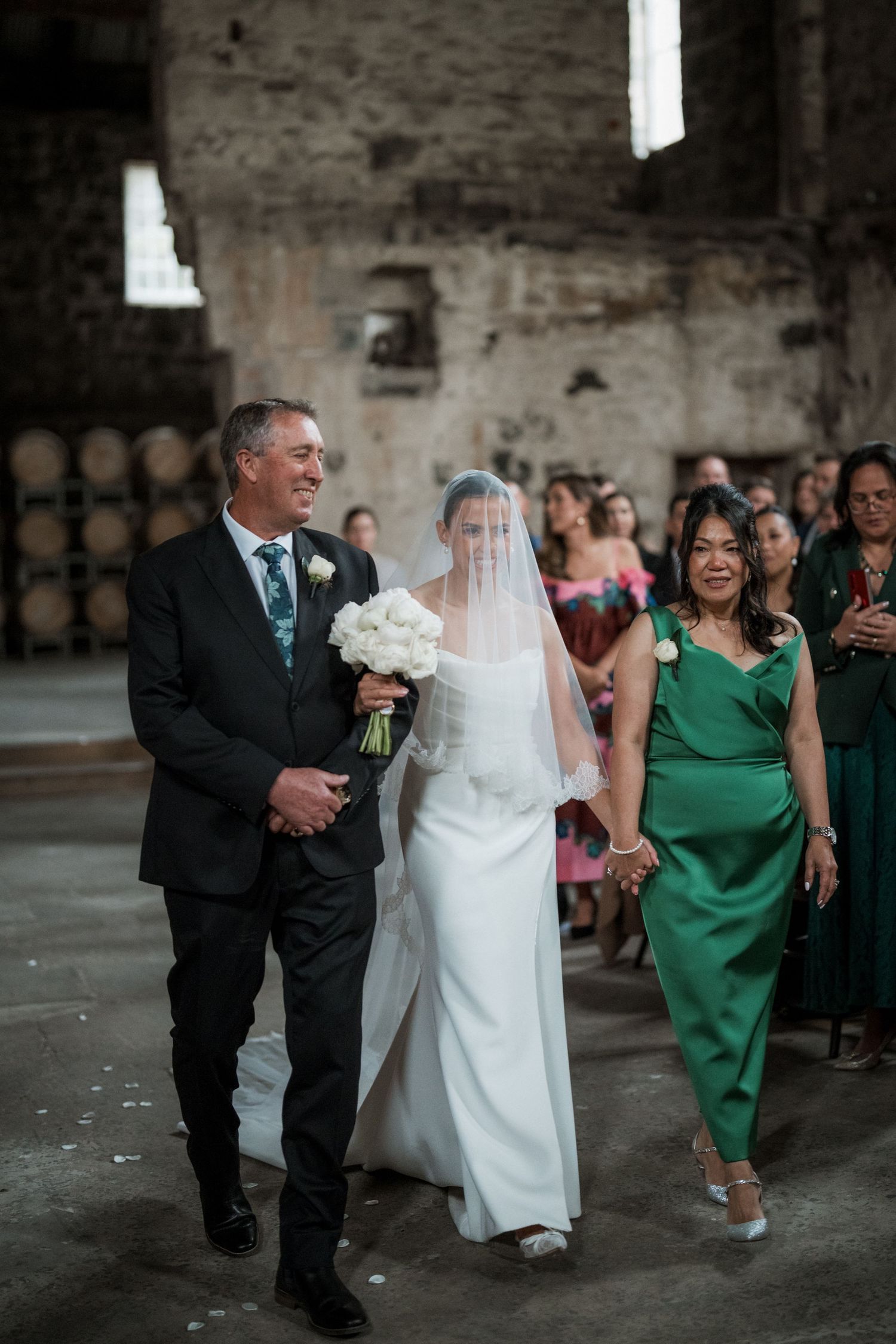 Wedding ceremony processional in rustic venue with exposed brick walls and wine barrels.