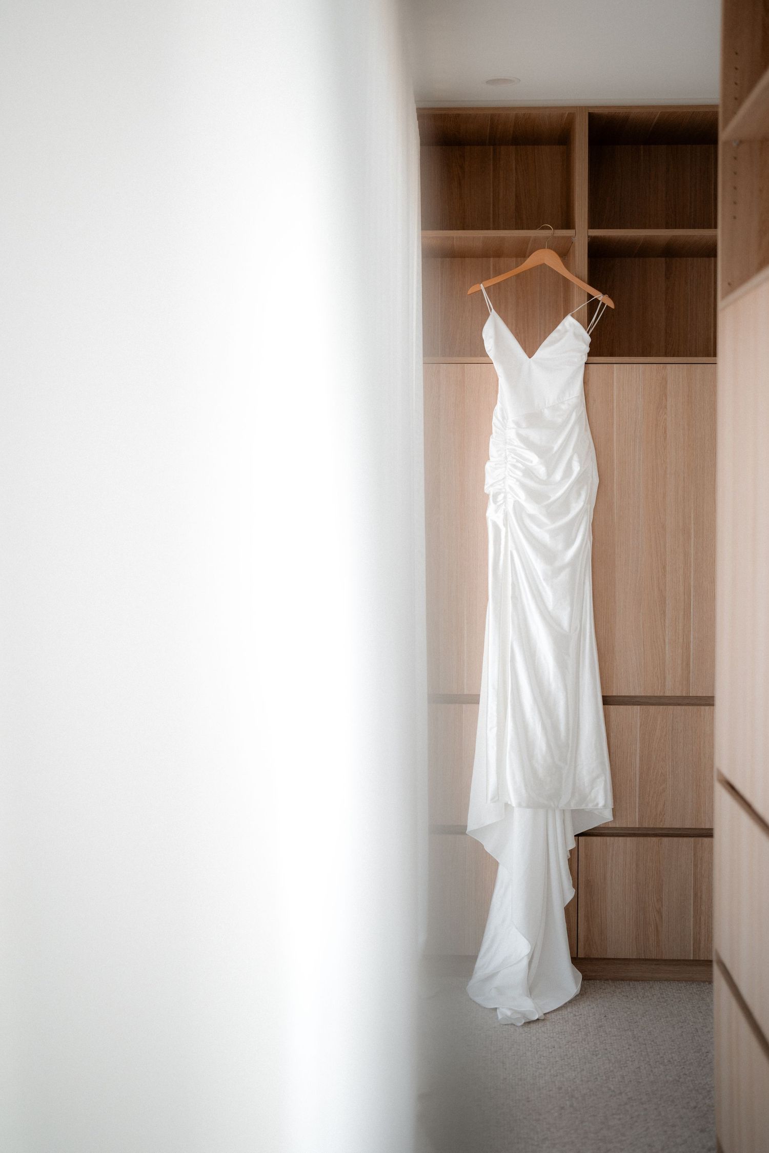 Series of white wedding dress photos hanging in a minimalist wooden closet with natural lighting.