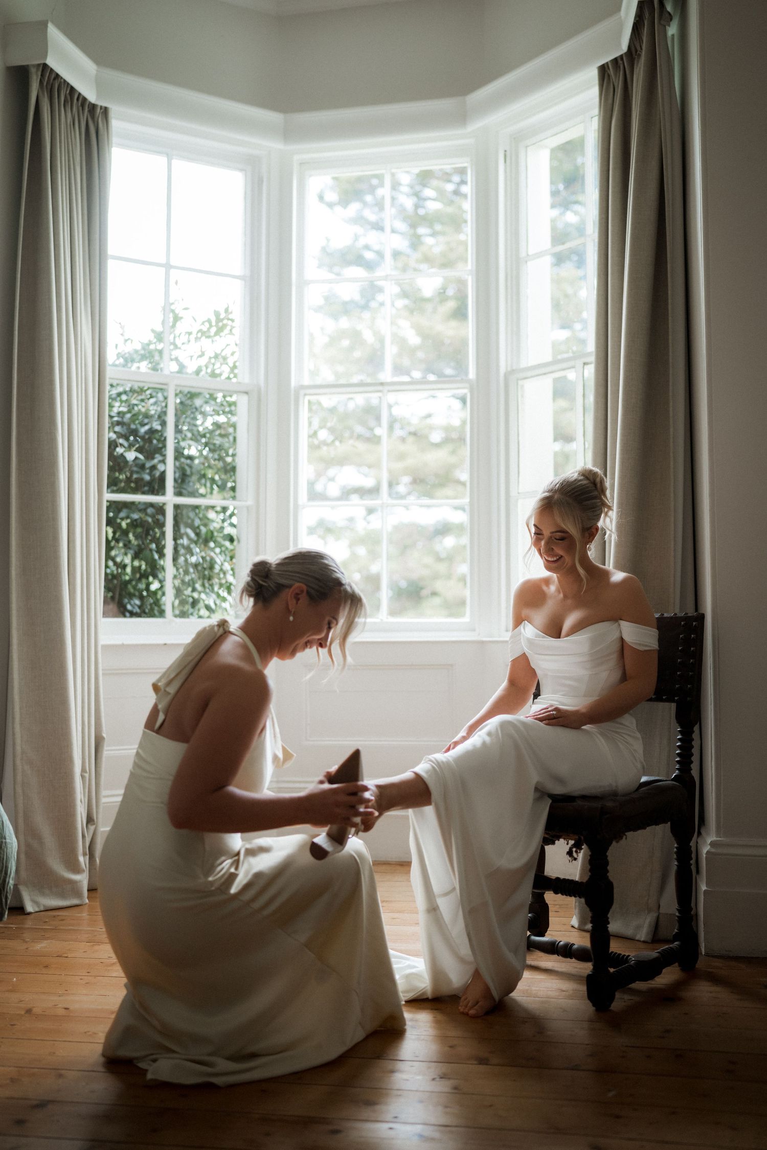 Wedding dress photos showing quiet moments in a sunlit room with large bay windows.