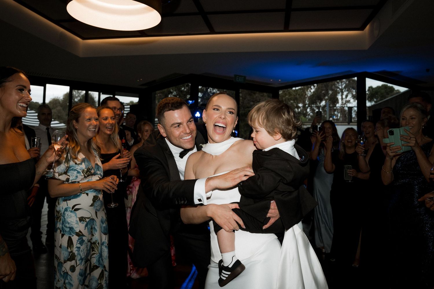 Joyful wedding reception moment with guests celebrating in an indoor venue with blue lighting.