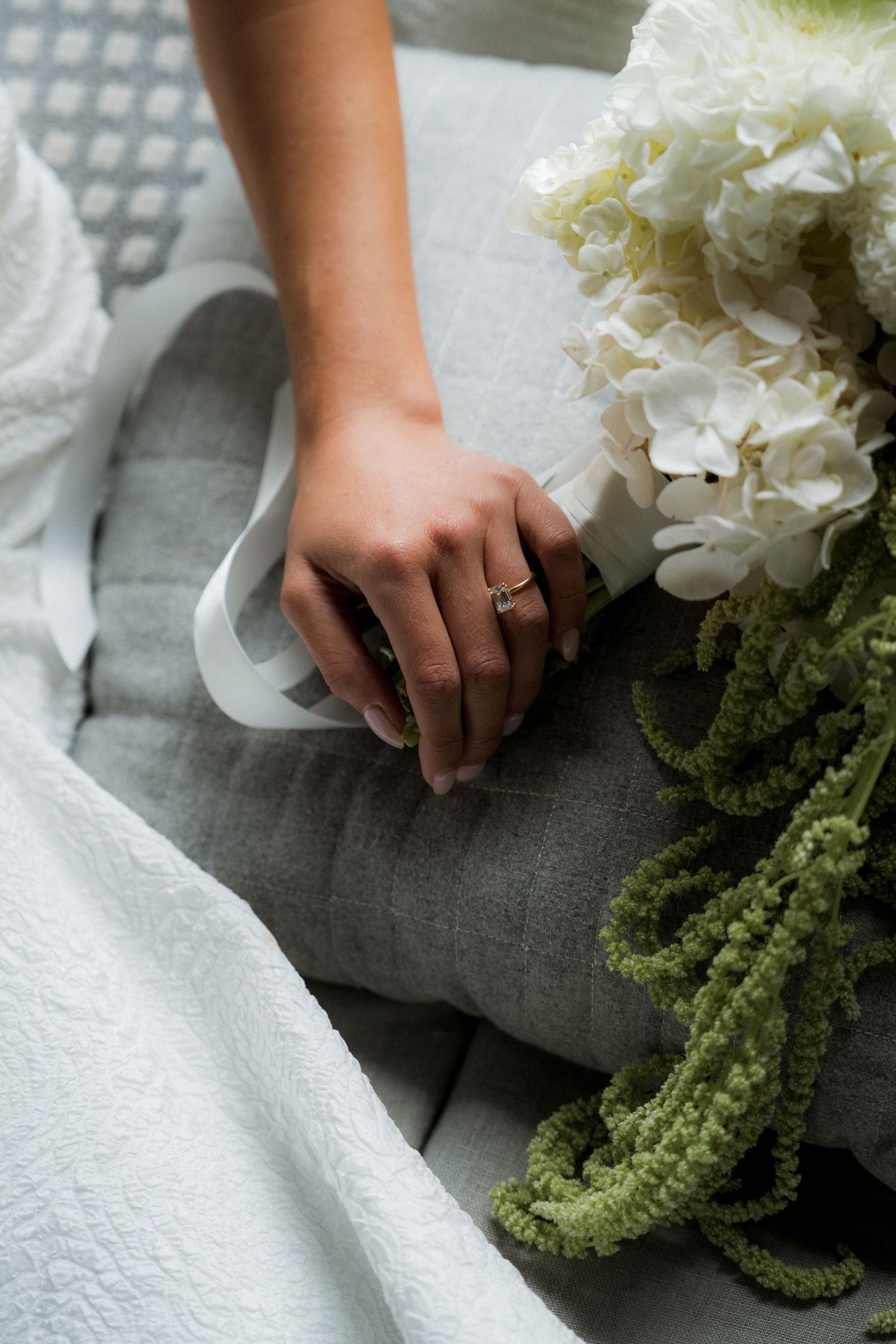 Close-up of bride's hand with engagement ring beside white hydrangea wedding bouquet.