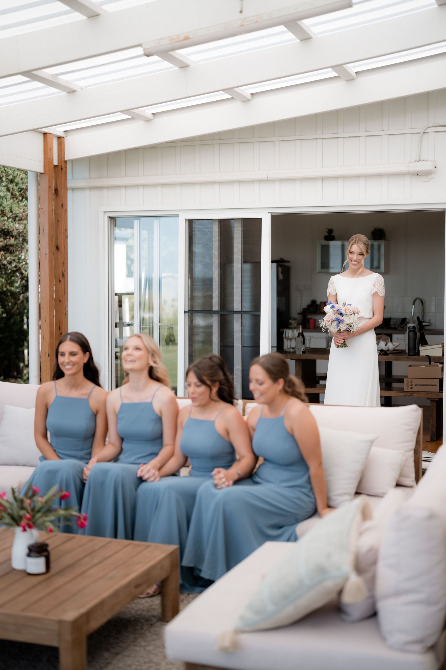 Wedding party on a patio featuring bridesmaids in dusty blue dresses seated on outdoor furniture.