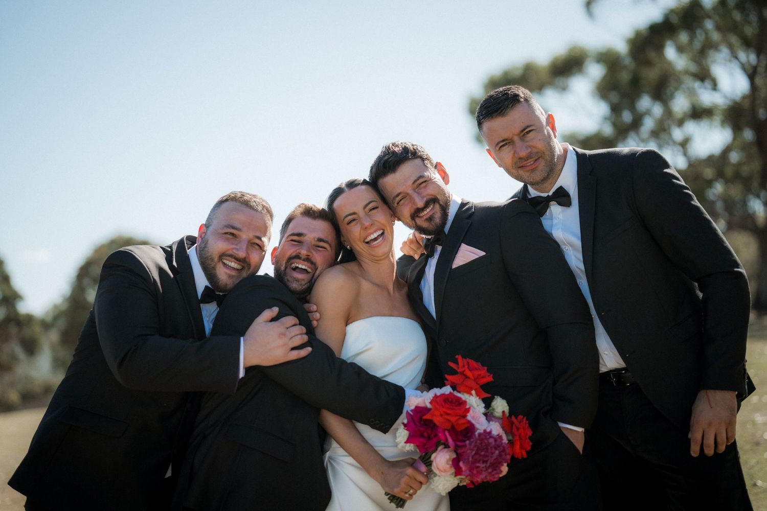 Wedding party members share candid laughing moments together during outdoor photo session.