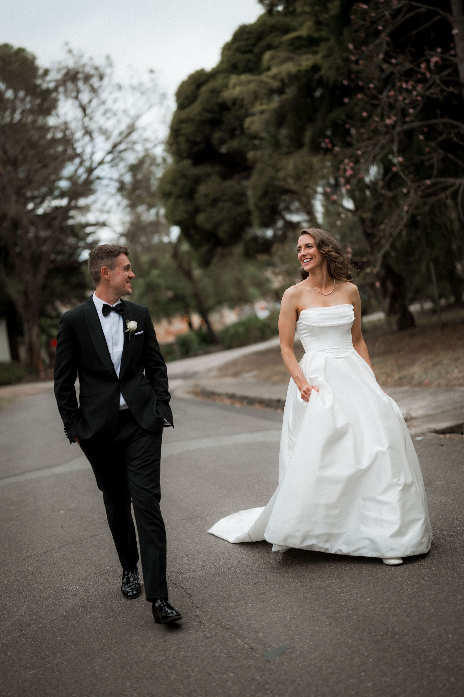 Newlyweds share playful moment on paved path during wedding photo session.