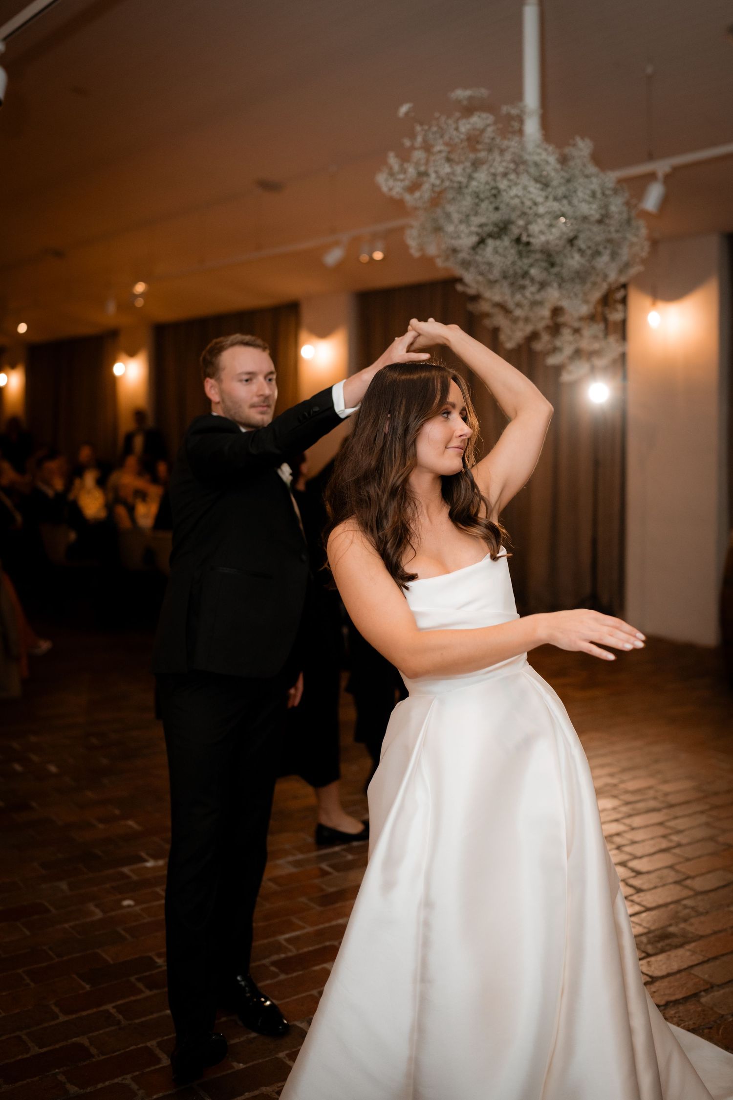 A couple dances together during their wedding reception with a baby's breath floral arrangement overhead.