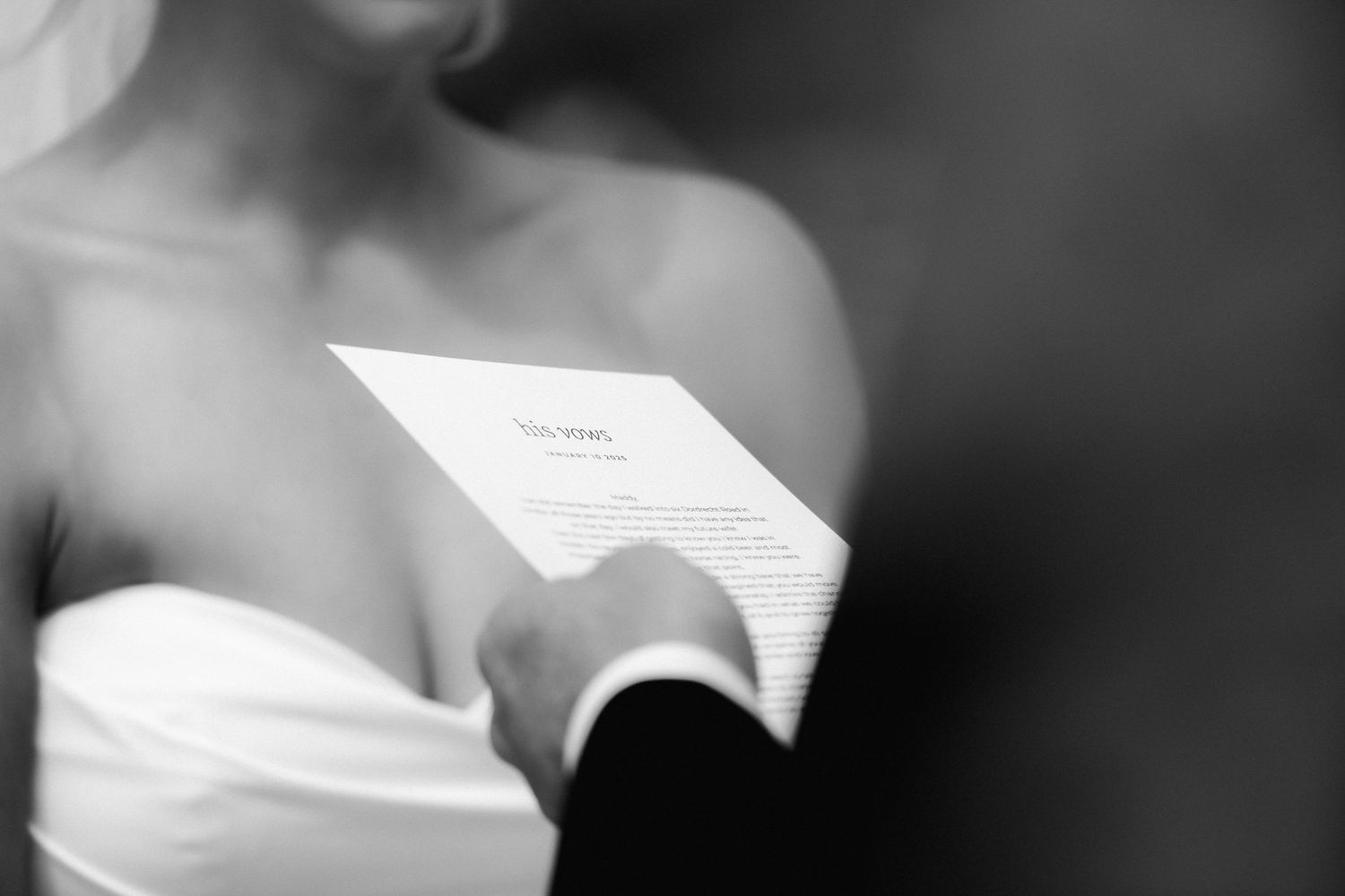 Black and white close-up shot of hands holding a wedding ceremony program or vows.