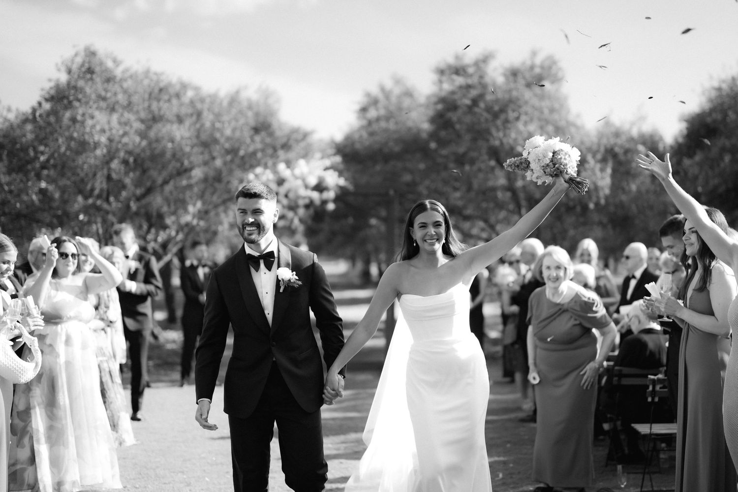Wedding party celebrates outdoors with joyful expressions and gestures.