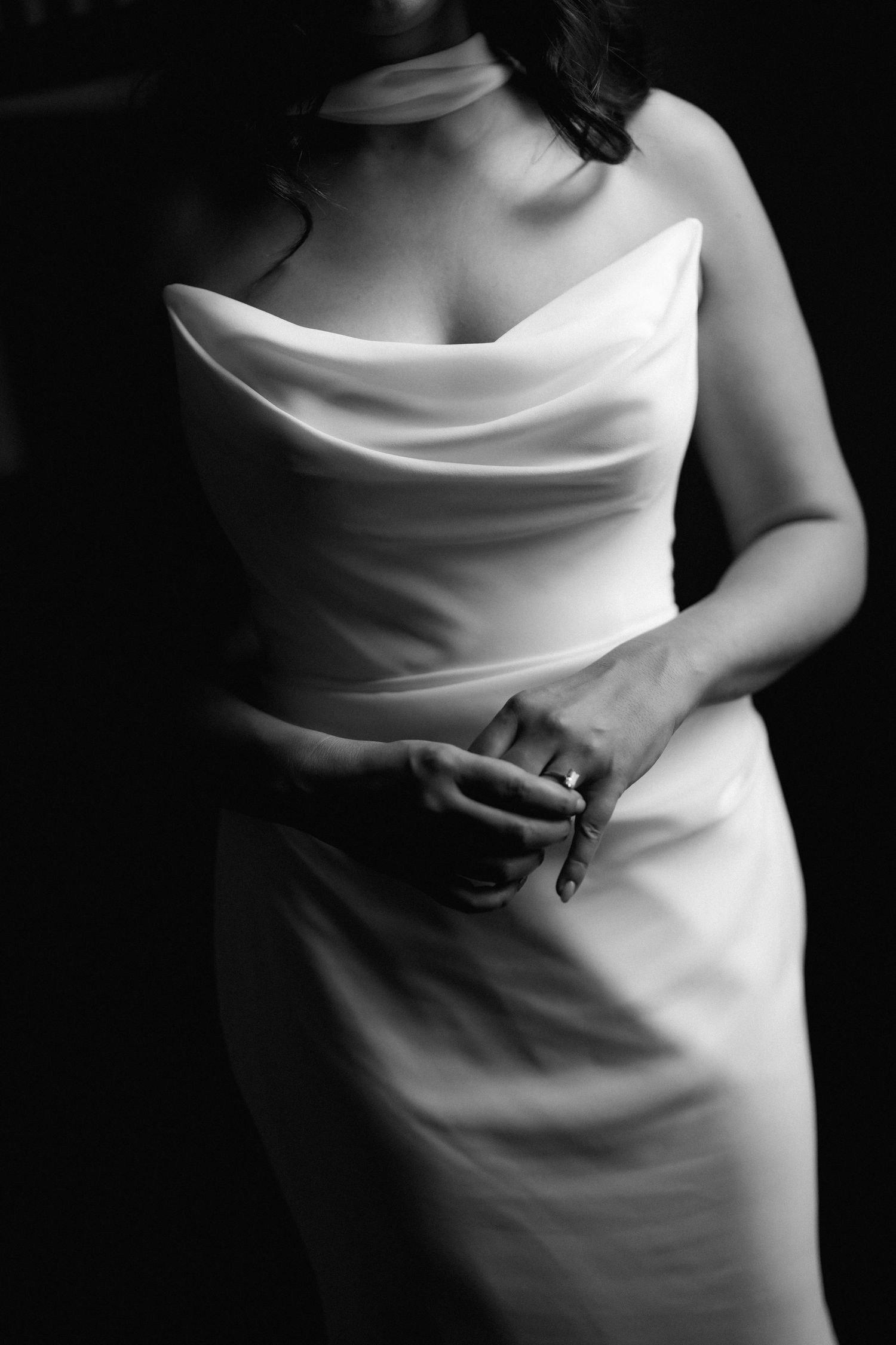 Black and white photo of a bride in elegant cowl neck wedding gown, hands clasped showing engagement ring.