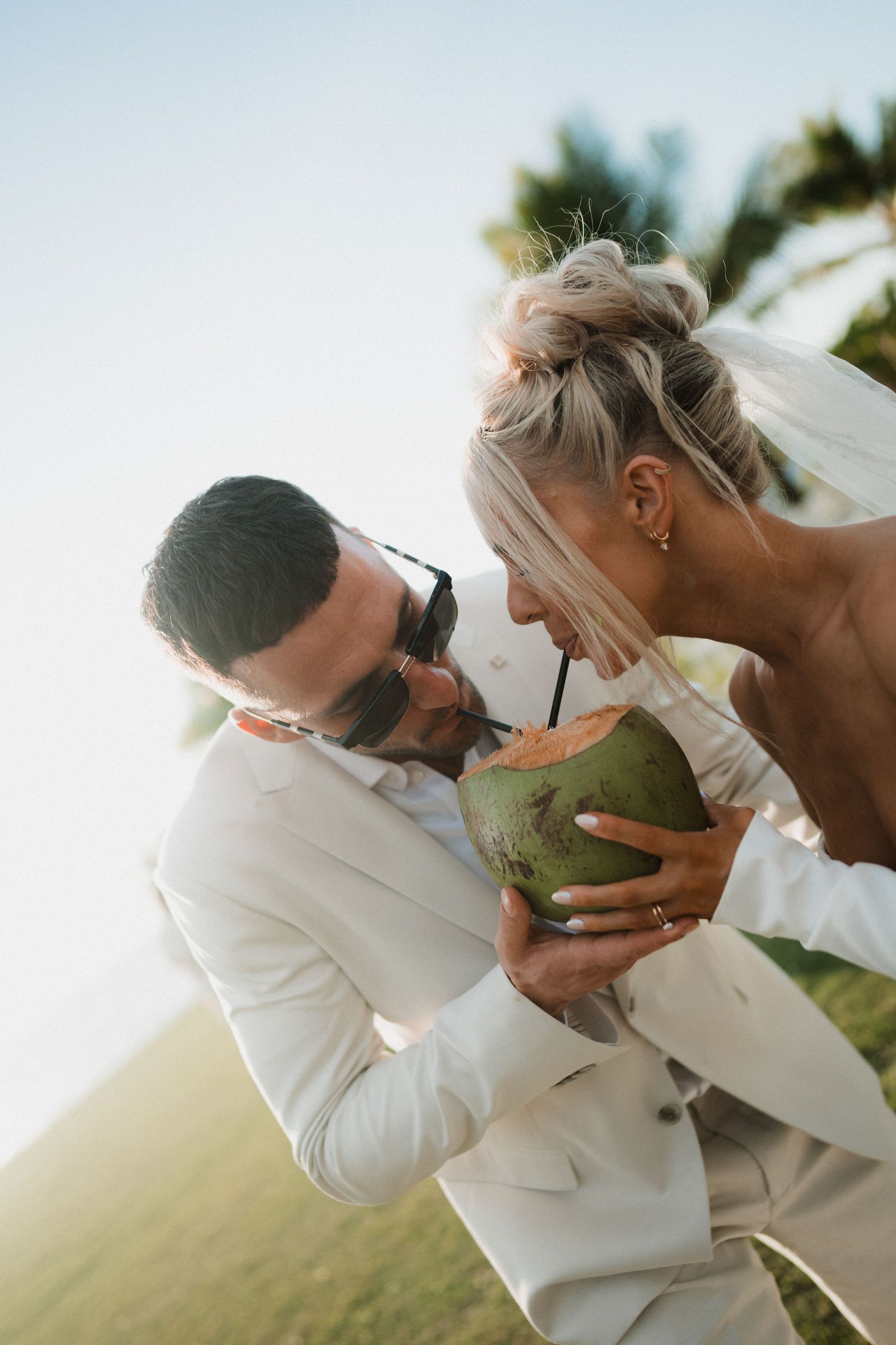 Couple sharing a fresh coconut drink together during a tropical wedding celebration.