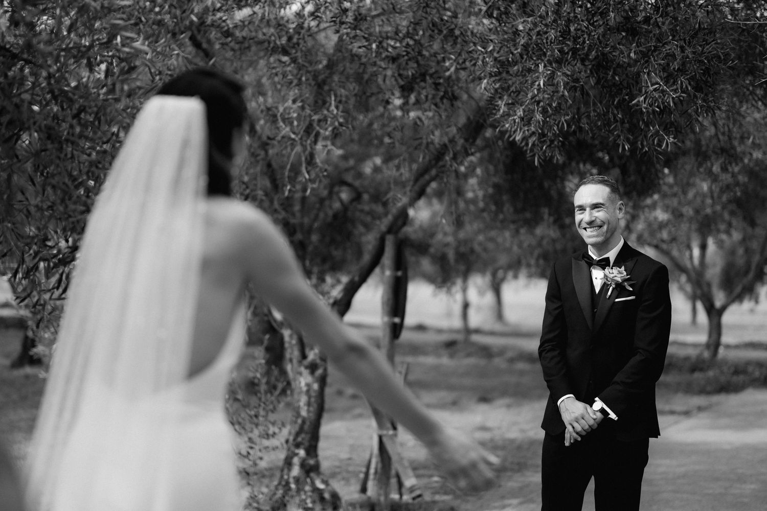 A black and white wedding photo showing a groom seeing his bride for the first time in an outdoor garden setting.