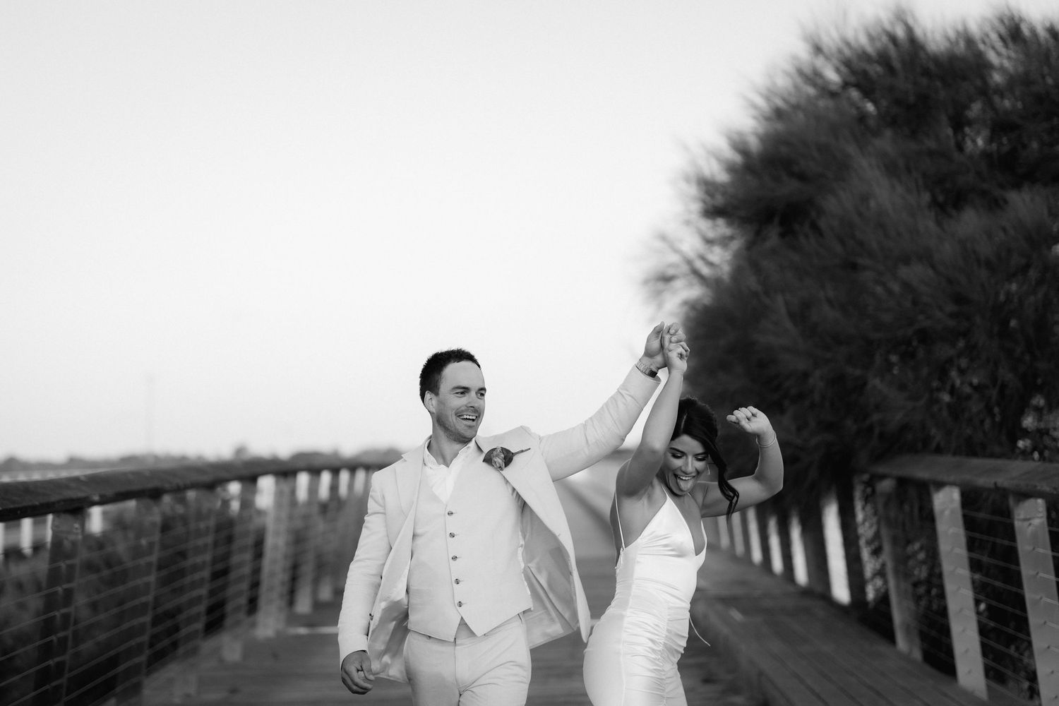 Wedding party walks along a tree-lined path during an outdoor photo session.