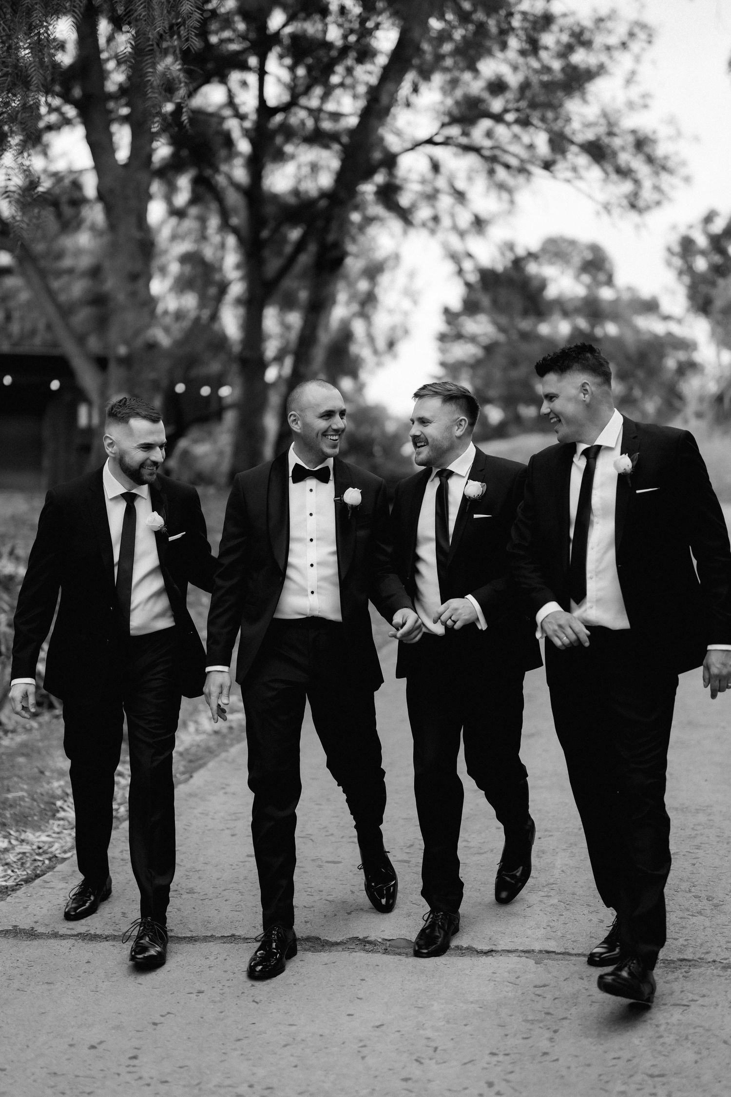A group of groomsmen in black suits walking and laughing together in a candid outdoor photo sequence.