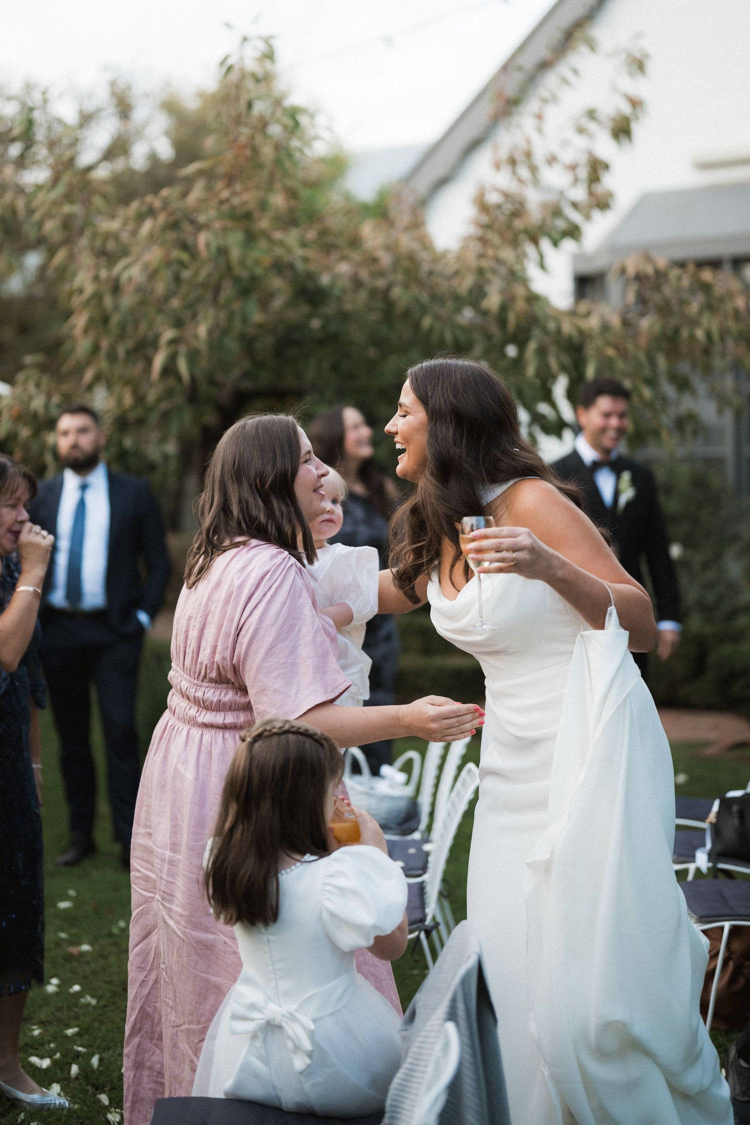 Wedding celebration on lawn with guests in pink dresses embracing and celebrating.