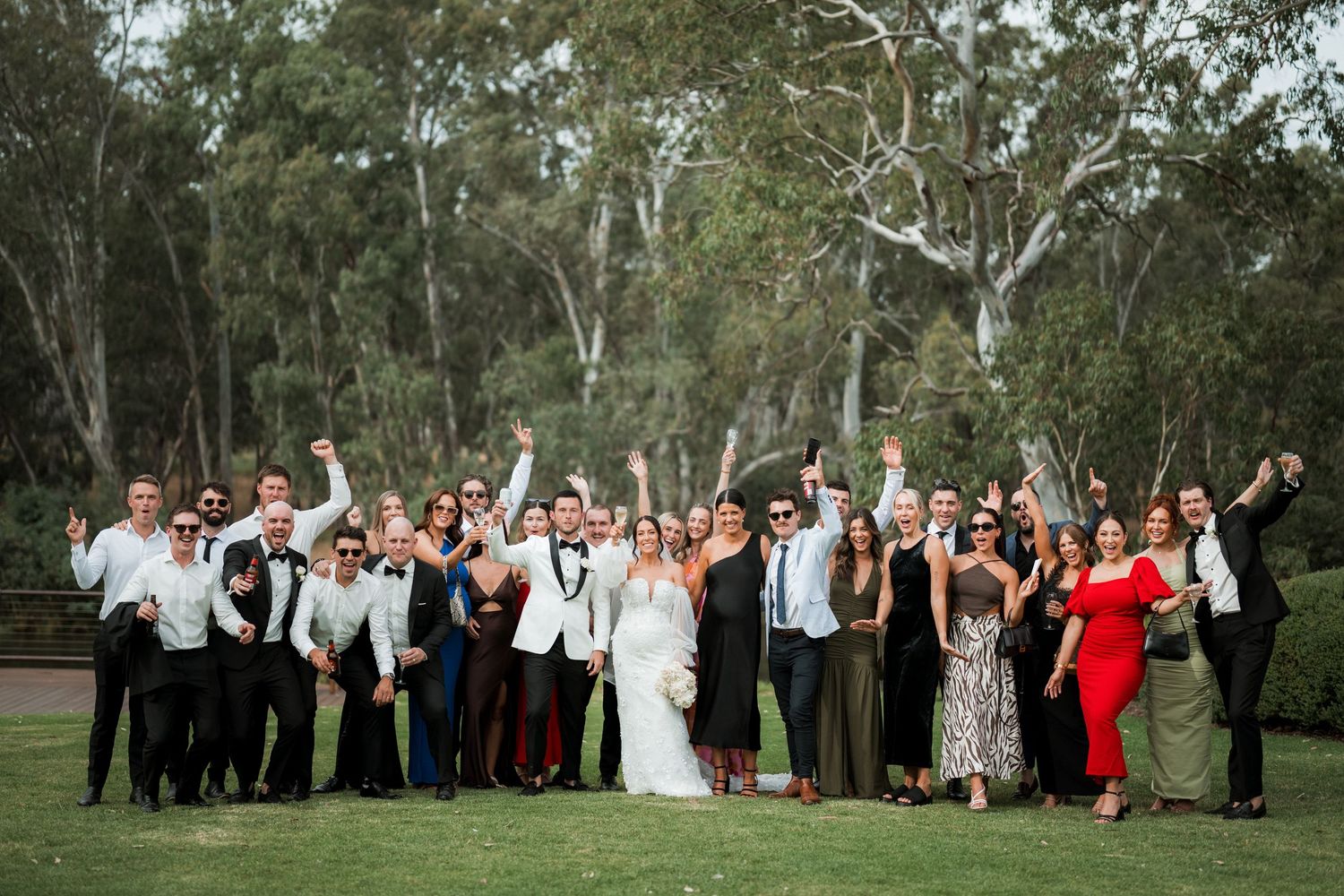 Wedding party poses together for a celebratory group photo outdoors among eucalyptus trees.