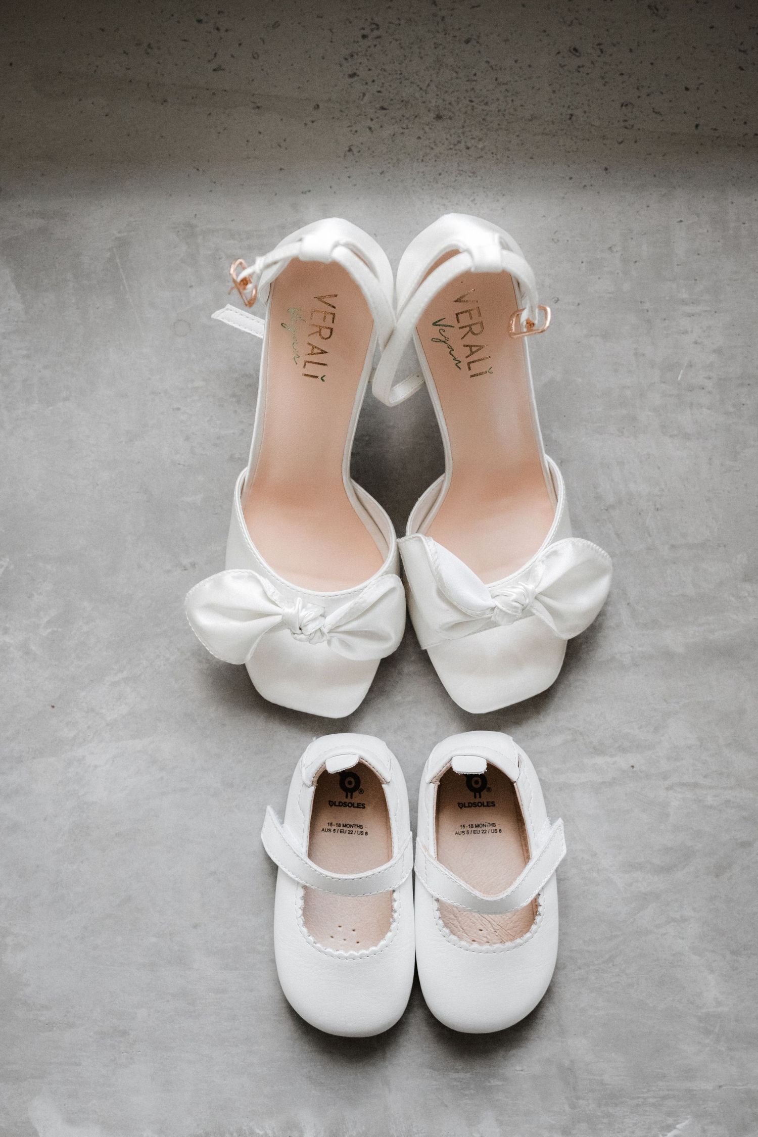 White baby shoes and ballet flats arranged on a gray concrete surface.