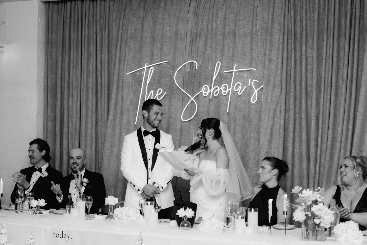 Wedding reception guests seated at long tables with white tablecloths and floral centerpieces during dinner service.
