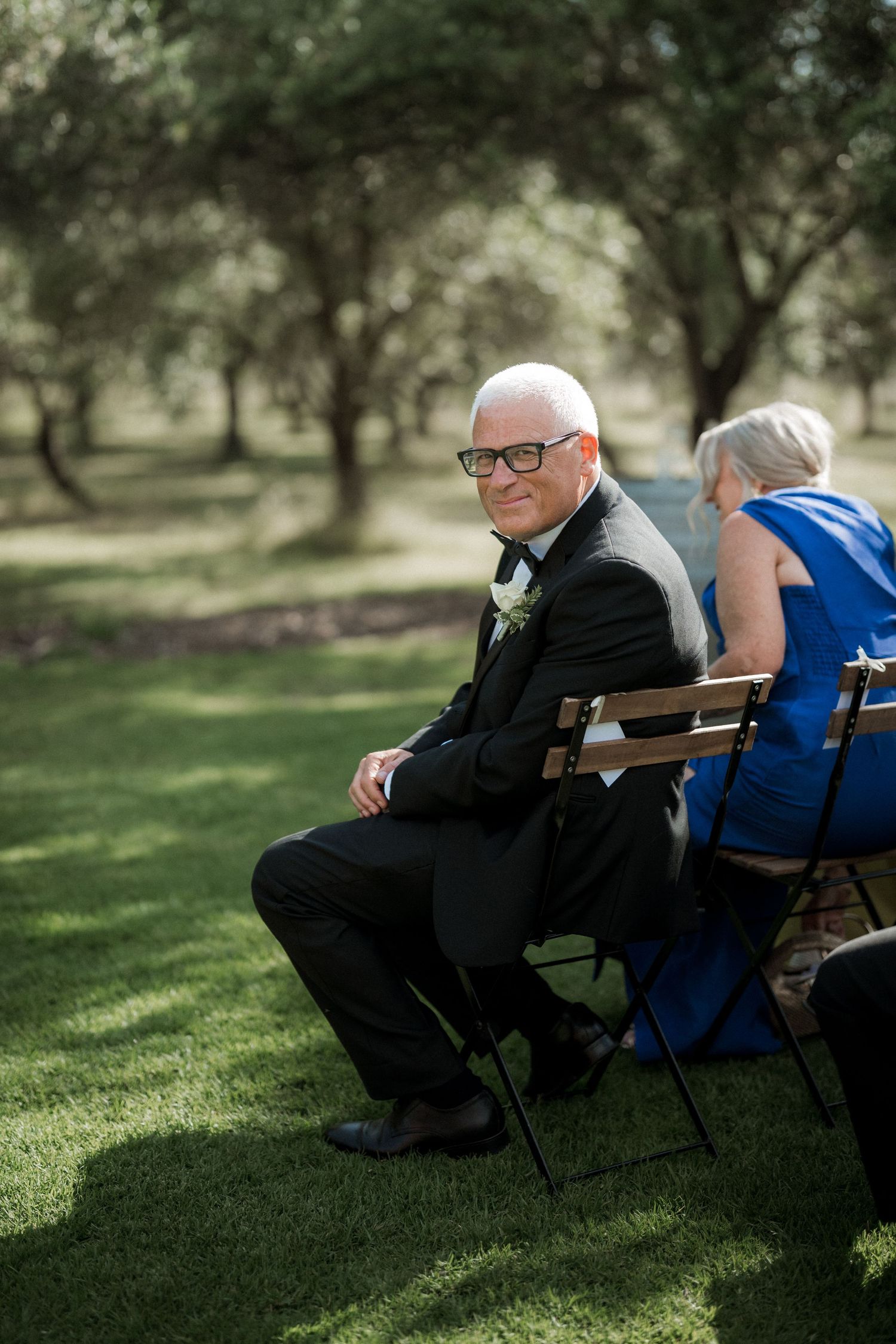 Wedding guests seated on folding chairs in a peaceful outdoor garden setting.