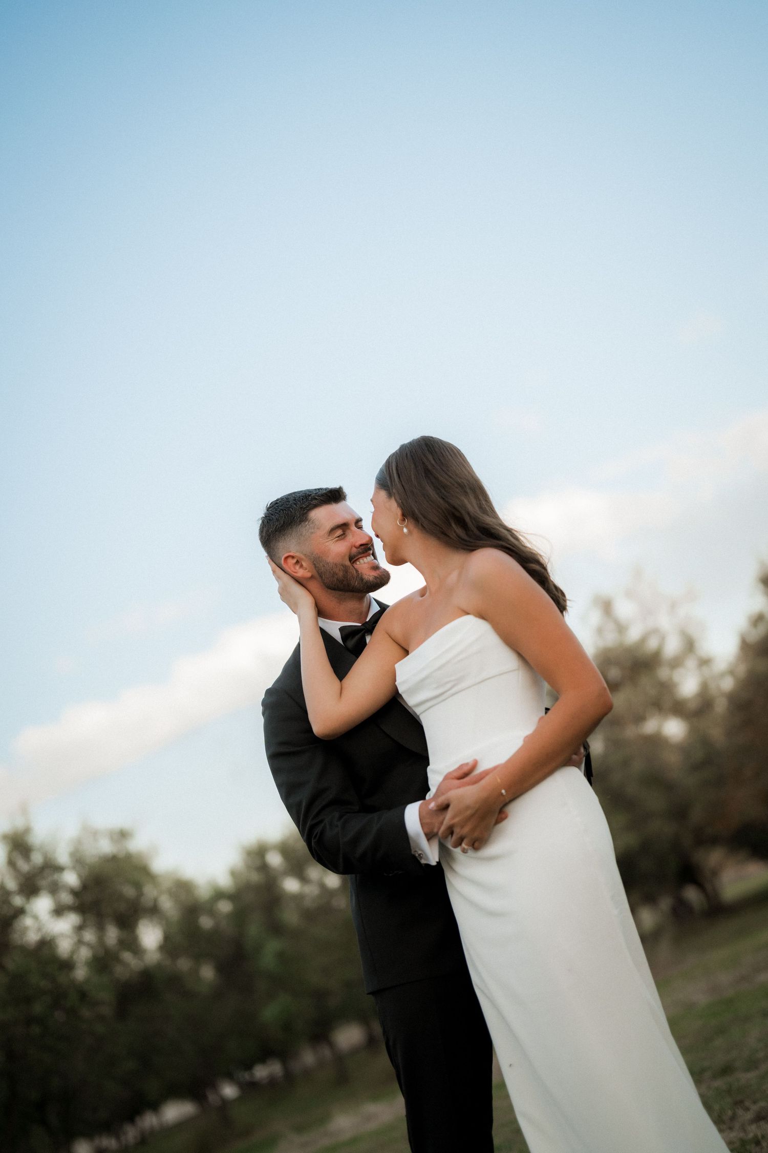 A romantic moment between newlyweds against a blue sky backdrop during their outdoor wedding photoshoot.