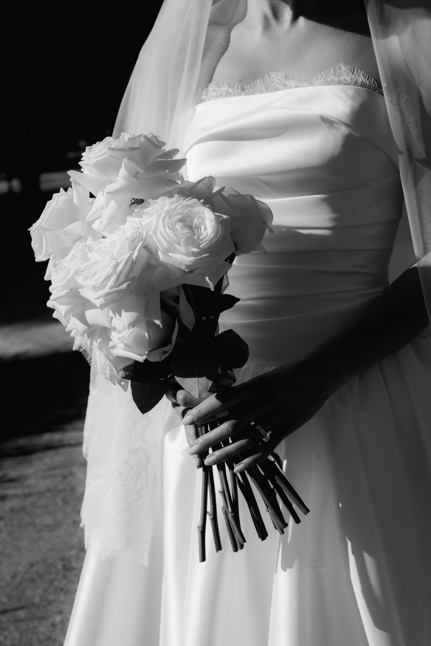 Black and white image of white rose wedding bouquets held against flowing dresses.