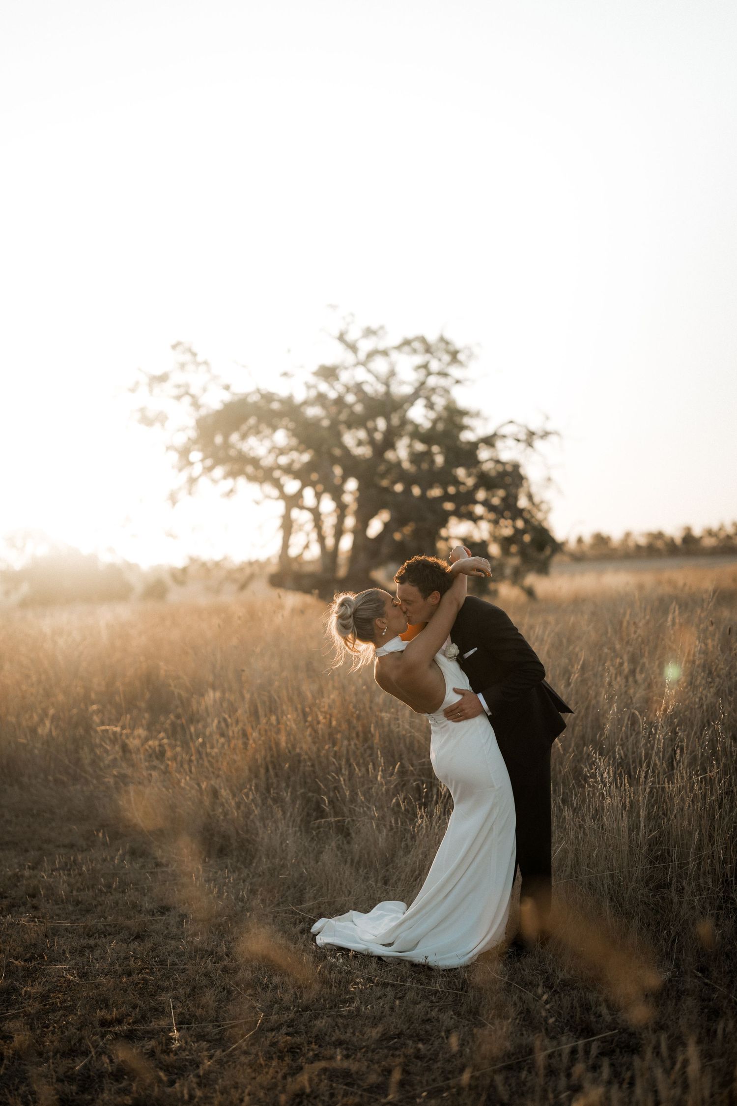 Artistic wedding photos of a couple dancing in a sun-lit field at golden hour.