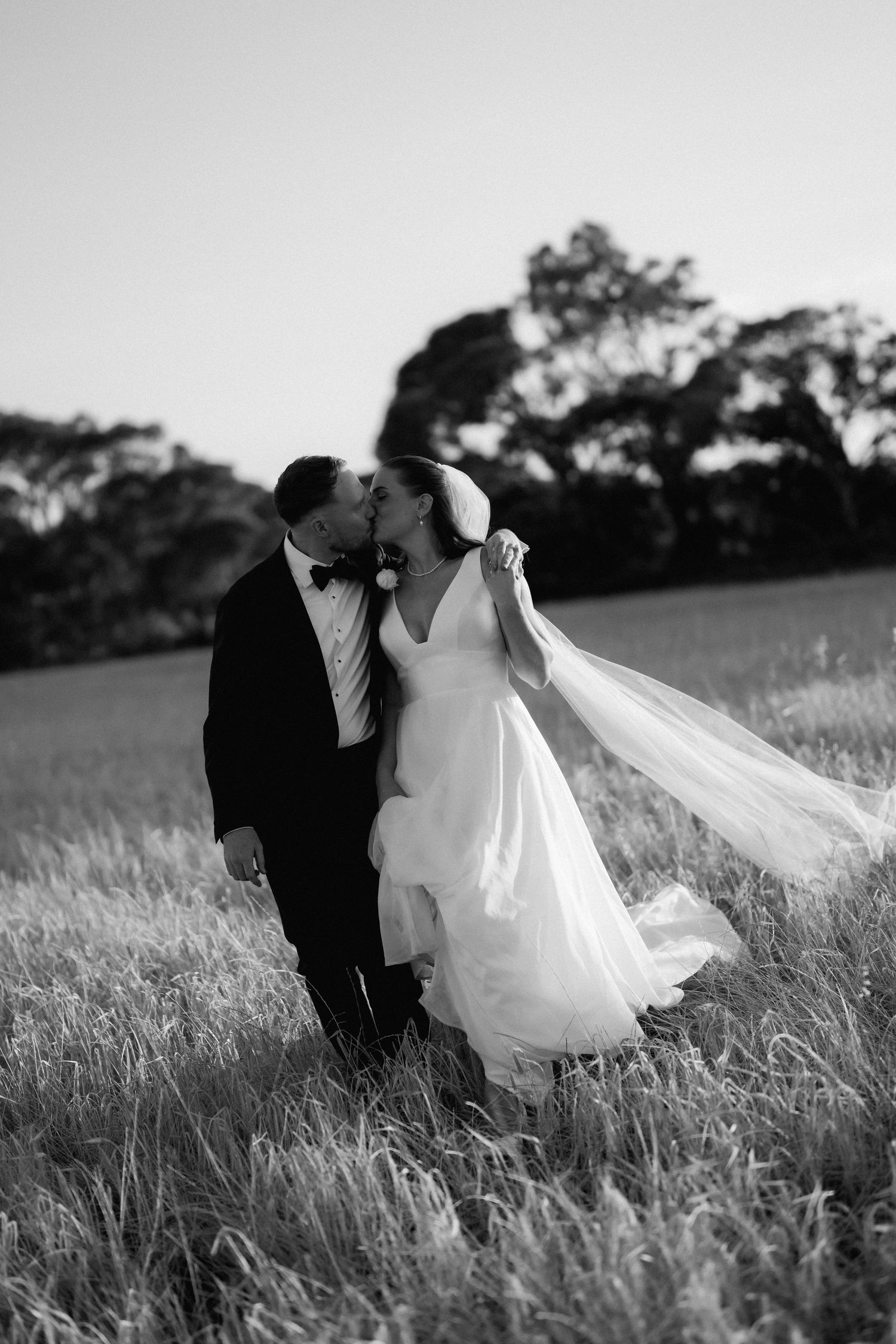 A black and white photo sequence shows a couple in wedding attire walking through a grassy field at sunset.