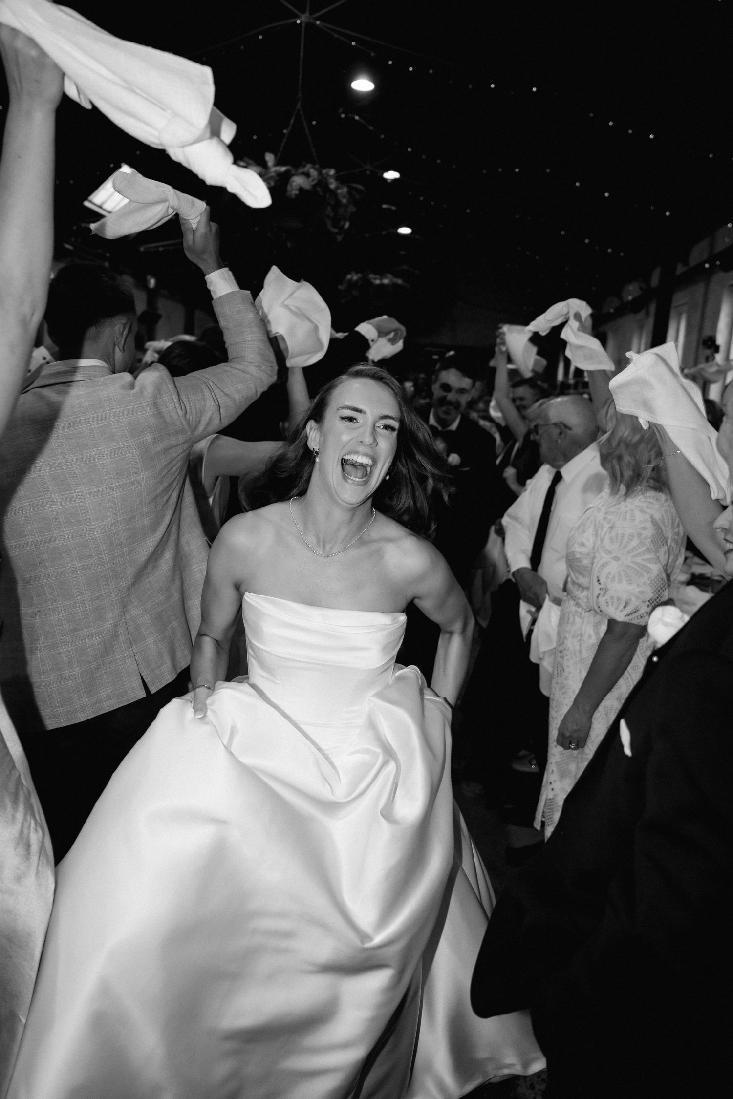 Wedding guests dancing and celebrating joyfully at a reception in black and white.