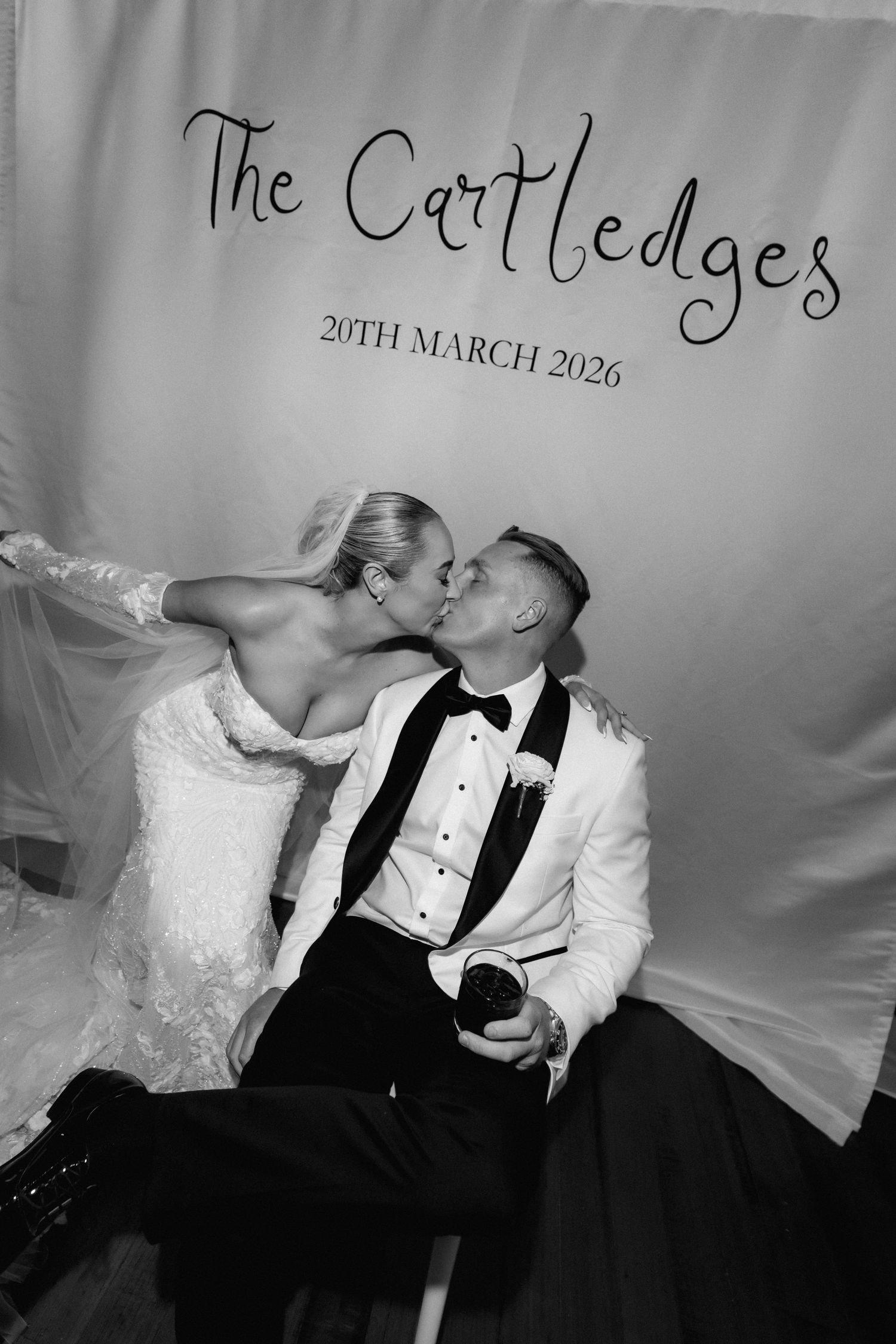 A black and white photo of a couple kissing at their wedding with 'The Cartledges' text backdrop.