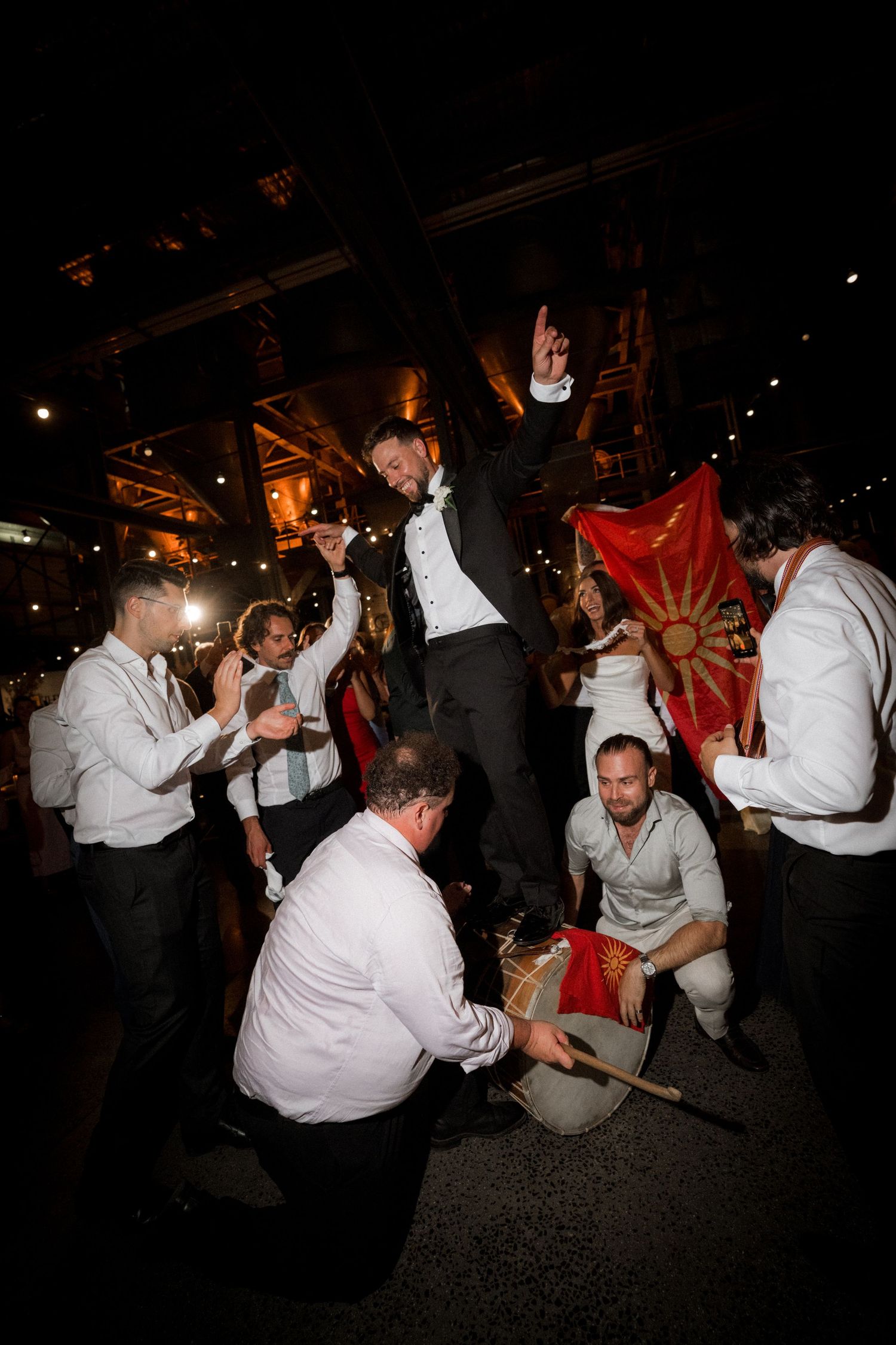 Wedding guests dancing energetically on a dark dance floor during a reception celebration.