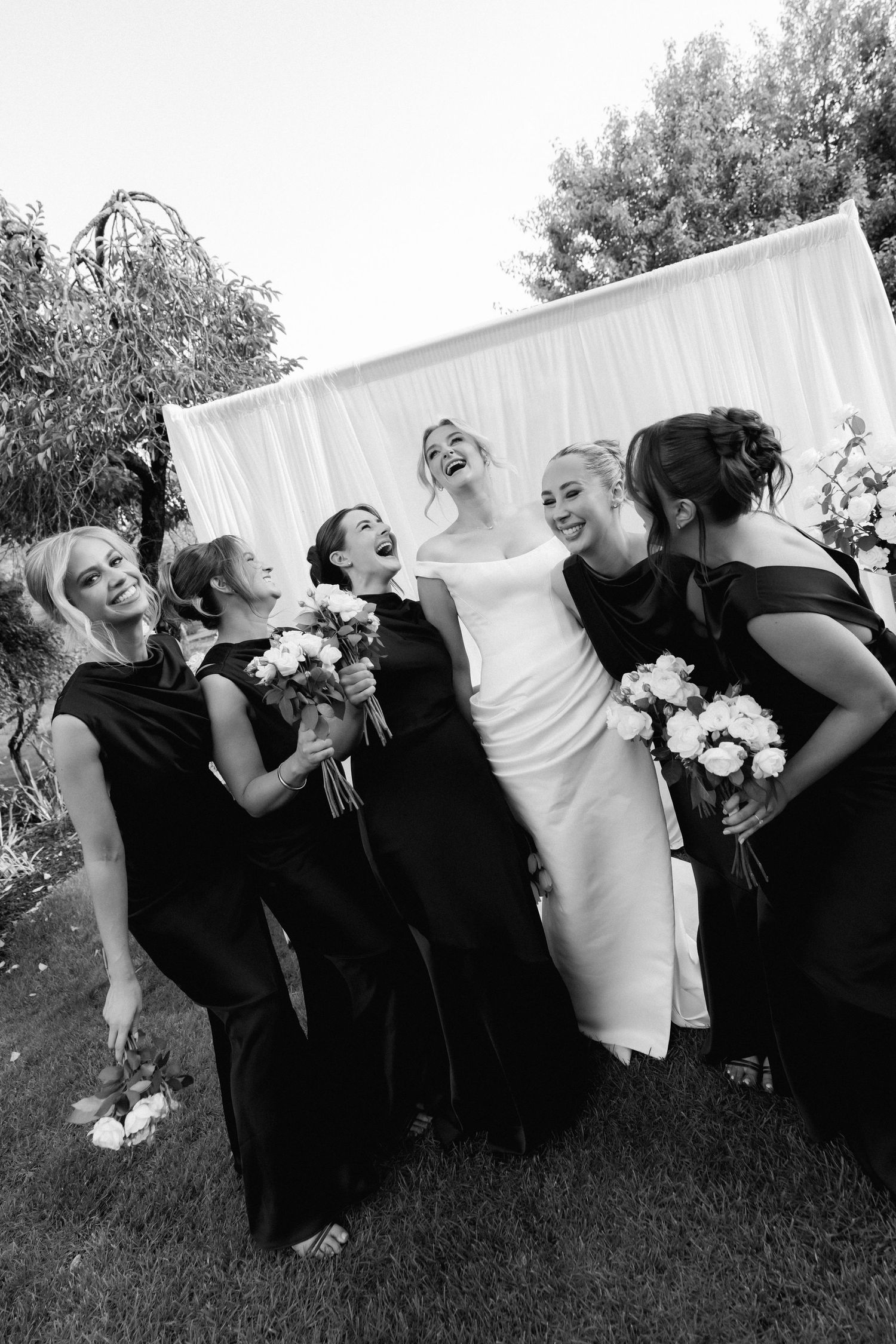Wedding party laughs and poses playfully behind white sheet in black and white photo series.