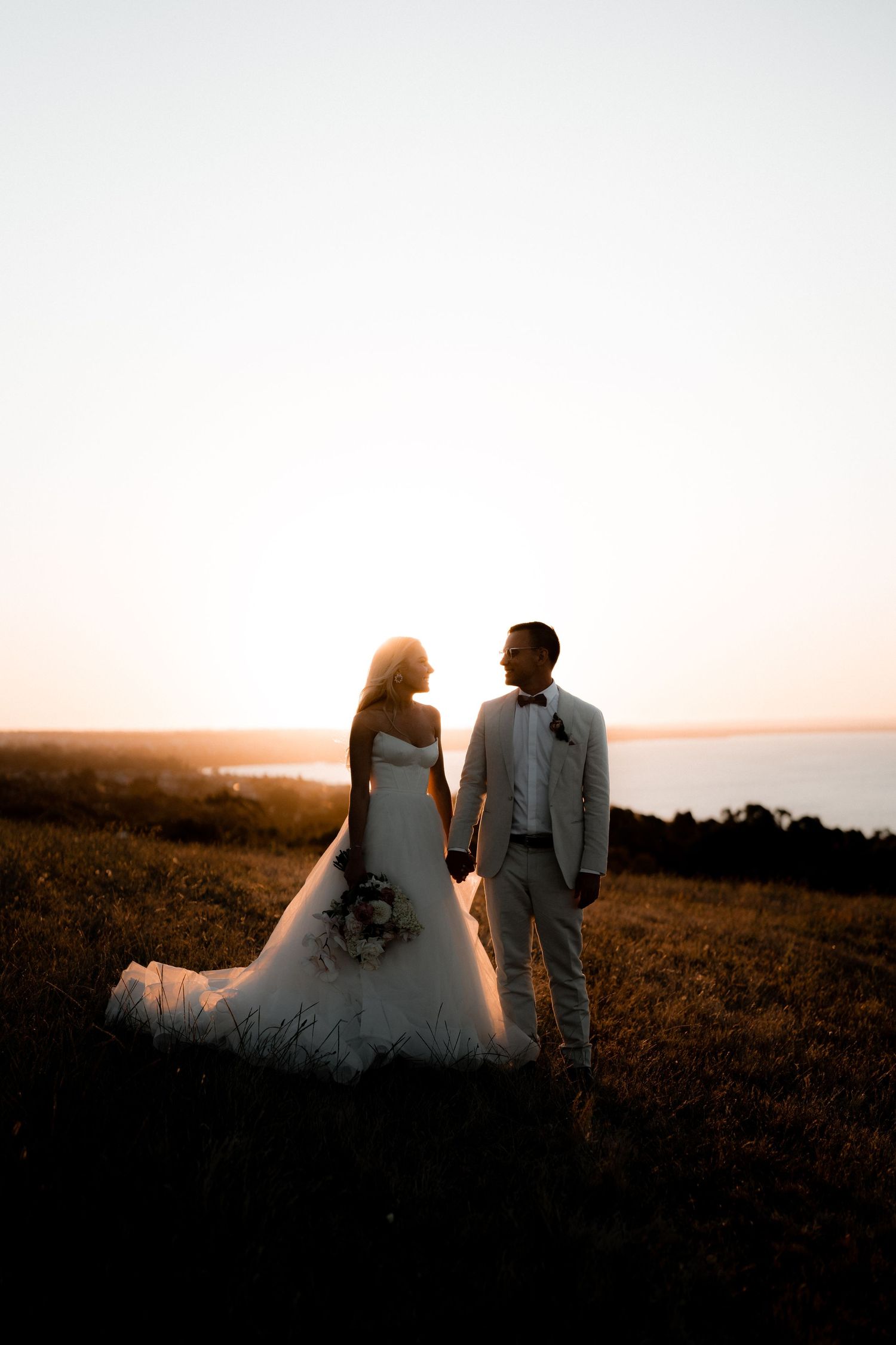 Silhouetted couple walking together at sunset after their wedding ceremony.