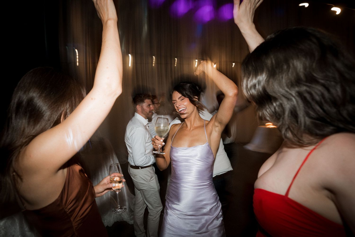 People dancing and celebrating at a dimly lit party with purple lighting effects.
