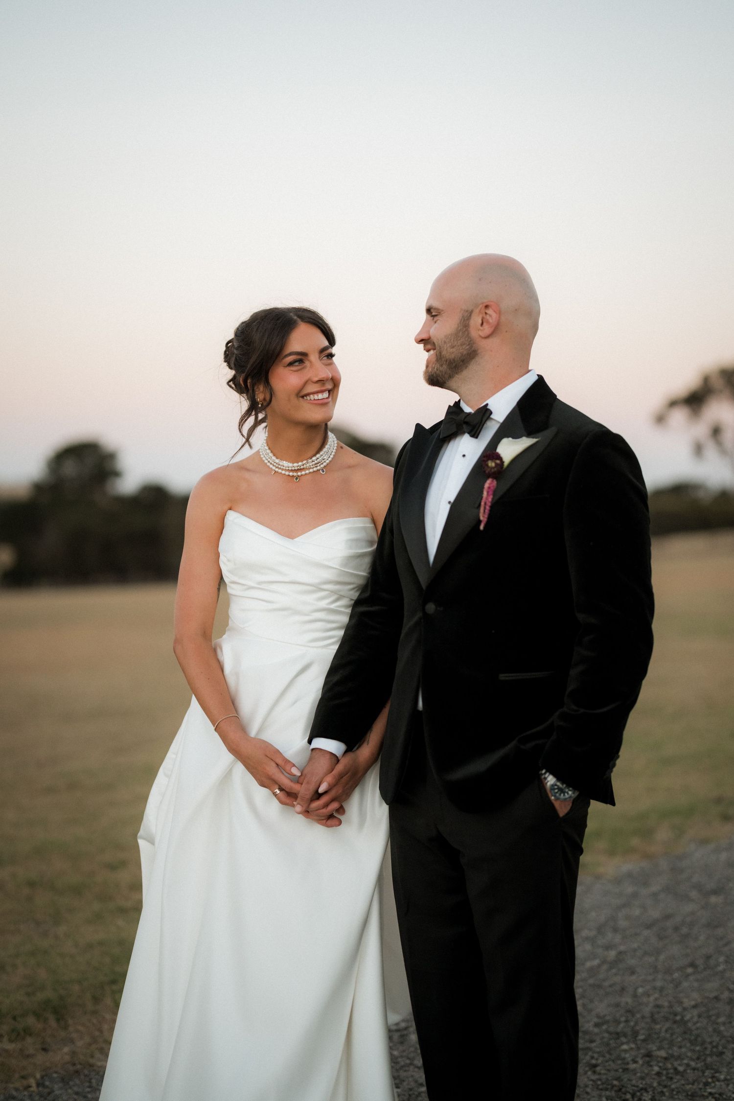 Wedding couple shares intimate moments in a field during golden hour while wearing formal attire.