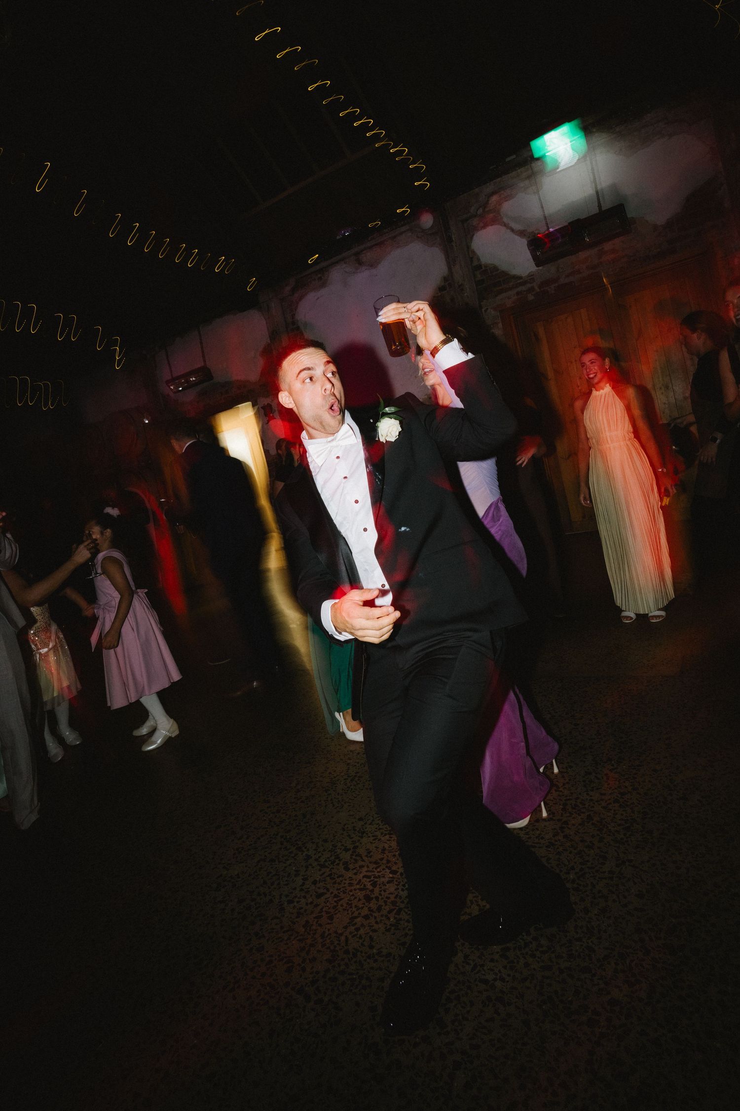 Silhouettes of wedding party members dancing at a dimly lit reception with colorful spotlights creating an energetic atmosphere.