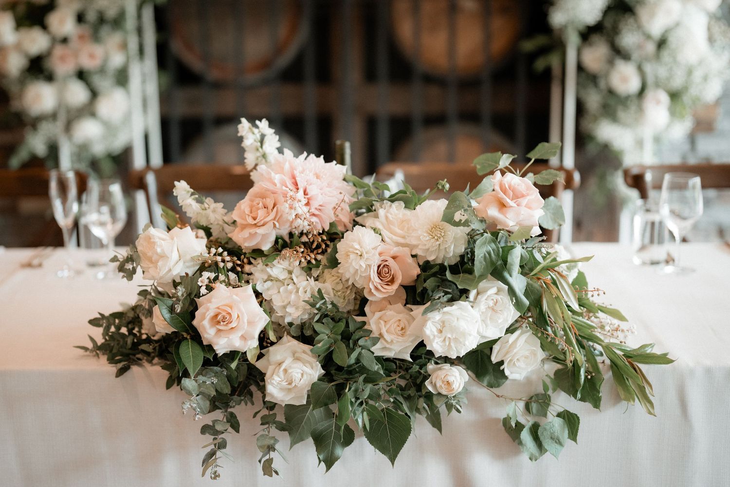 Elegant blush pink and white rose floral centerpiece with cascading greenery on white tablecloth at wedding reception.