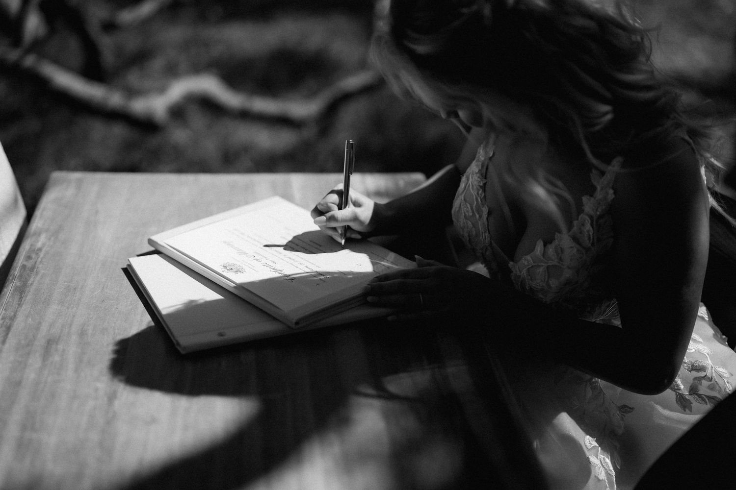A student writes in a notebook at a wooden desk in a black and white photograph.