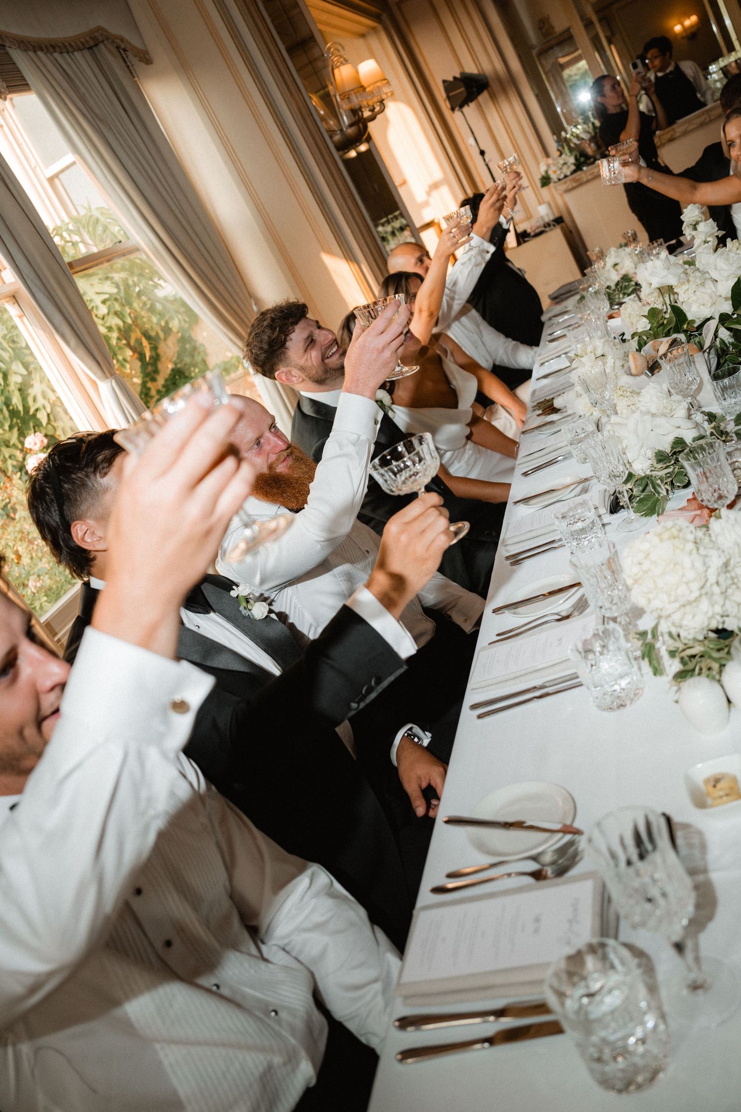 Wedding guests raise their glasses in celebration at an elegant reception dinner table.